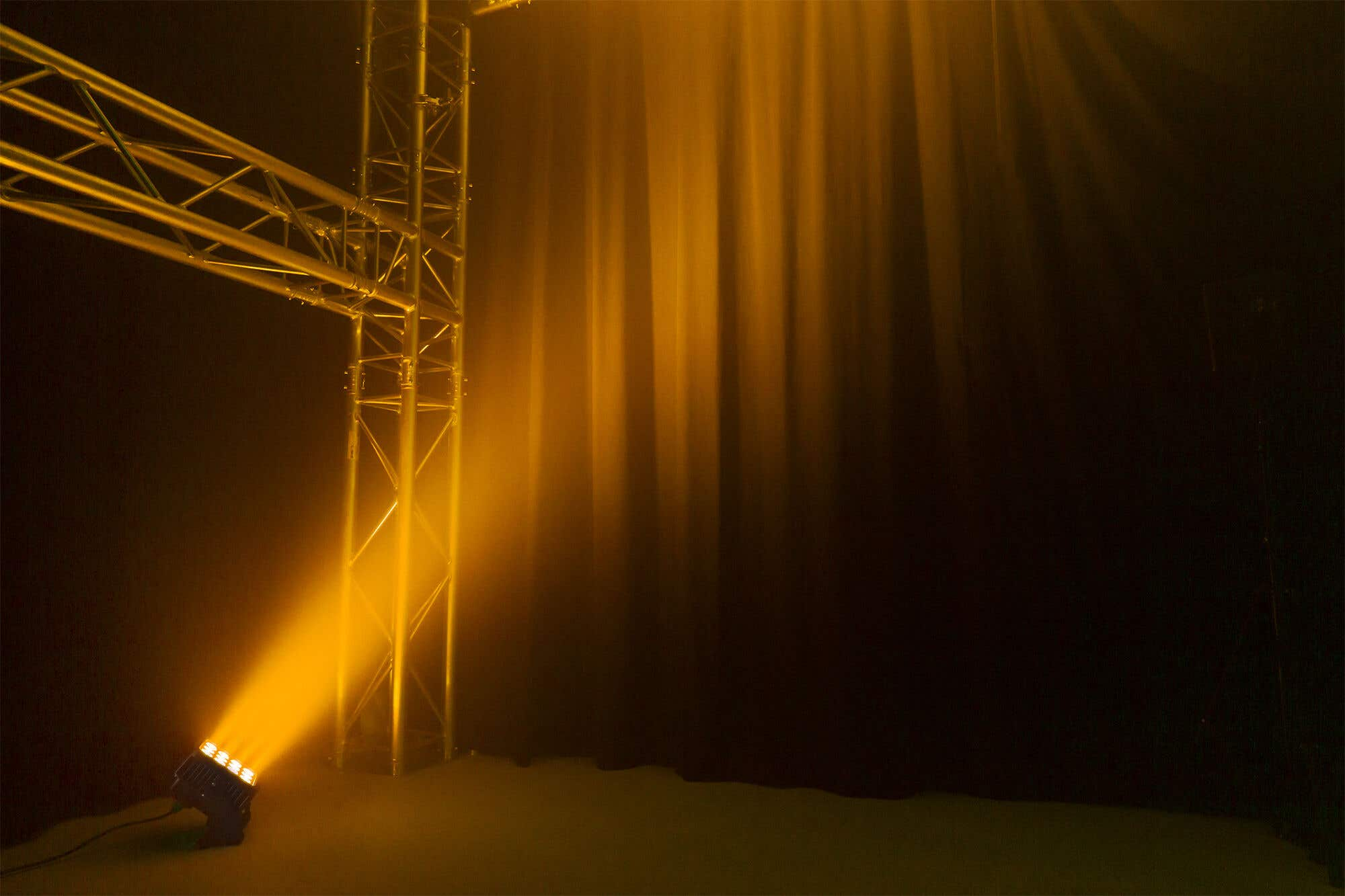 Una puesta en escena con un foco que ilumina una estructura metálica. El fondo es una cortina oscura y la luz es amarilla.