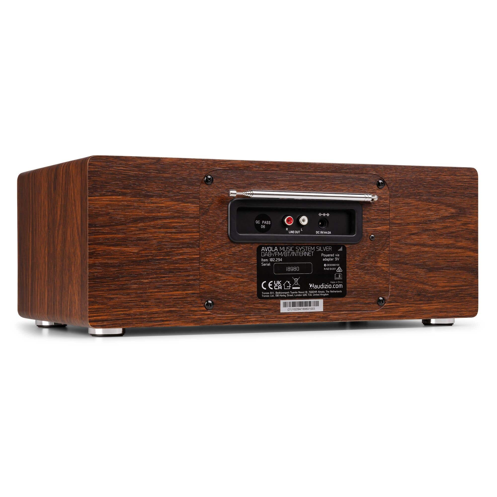 Vue arrière d'une radio en bois. Elle comporte des ports, une petite antenne et des étiquettes. Pieds argentés.