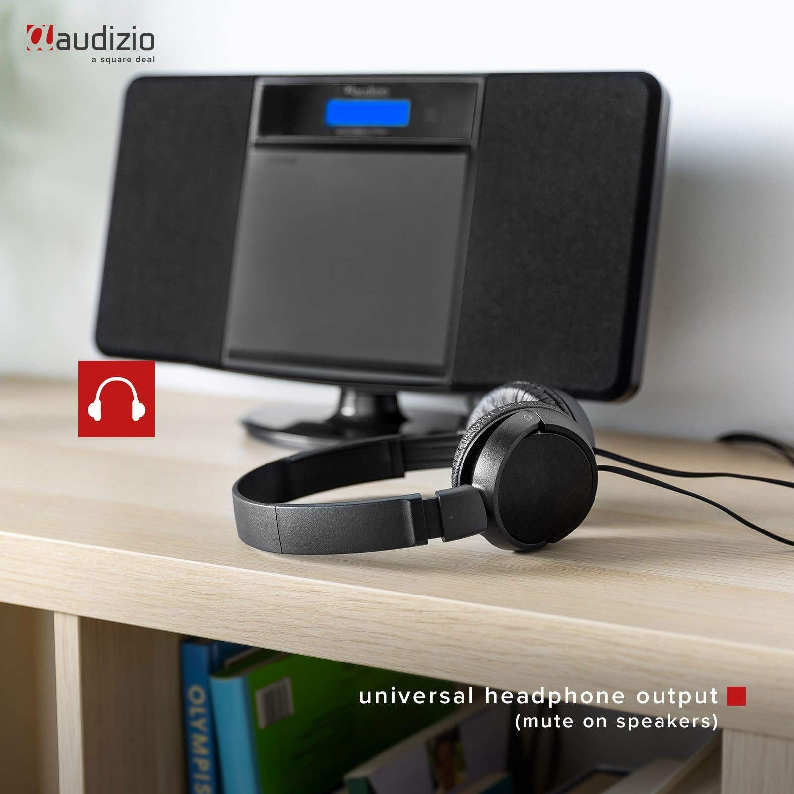 Sistema estéreo negro con auriculares sobre una mesa de madera. Libros visibles al fondo.