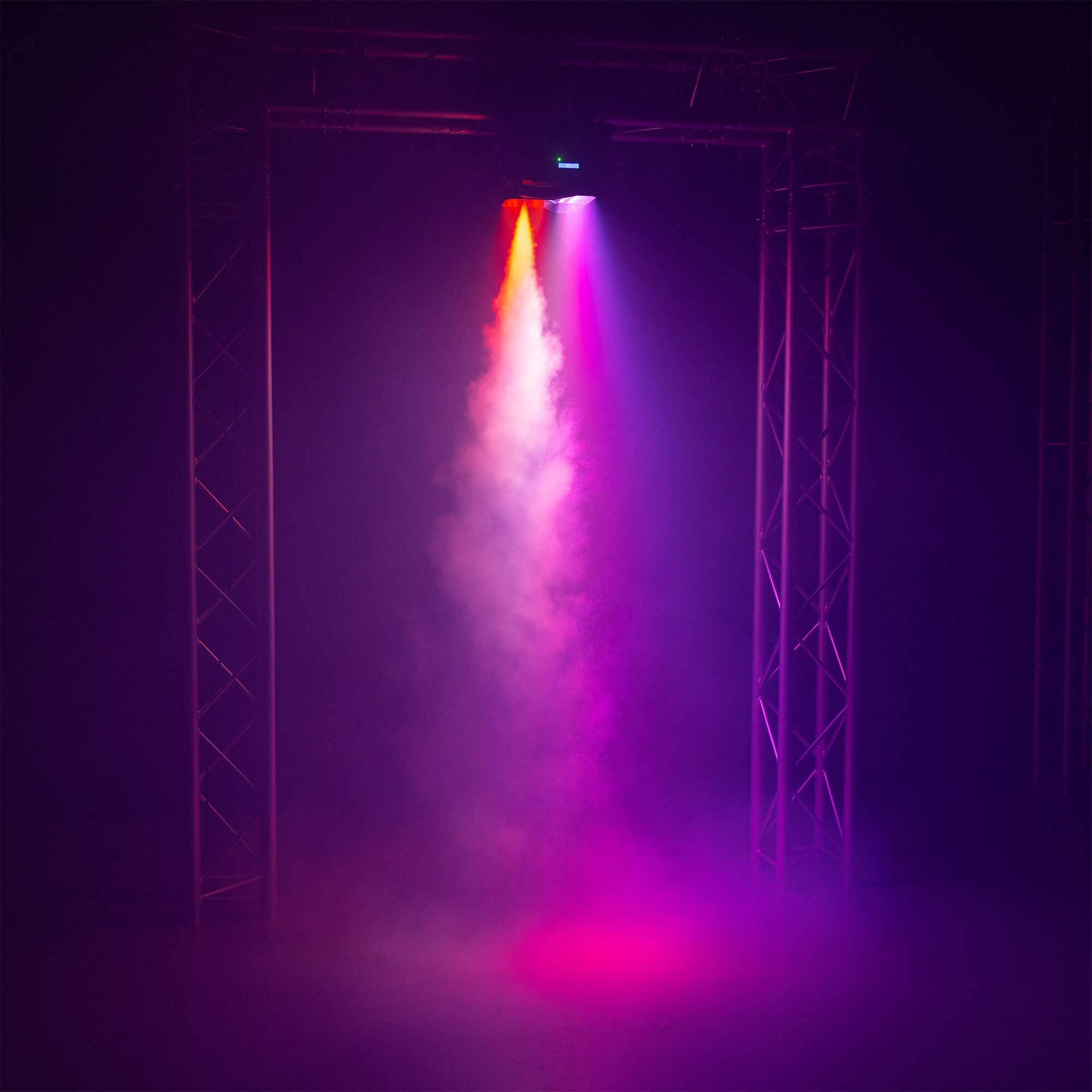 Montaje de iluminación de escenario con trusses y haces de luz naranja y rosa, humo. Fondo púrpura oscuro.