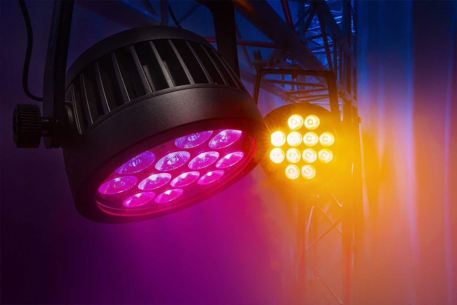 Dos luces de escenario con colores vibrantes. Una es morada, la otra amarilla. Ambas están sobre una estructura metálica, con fondo oscuro.