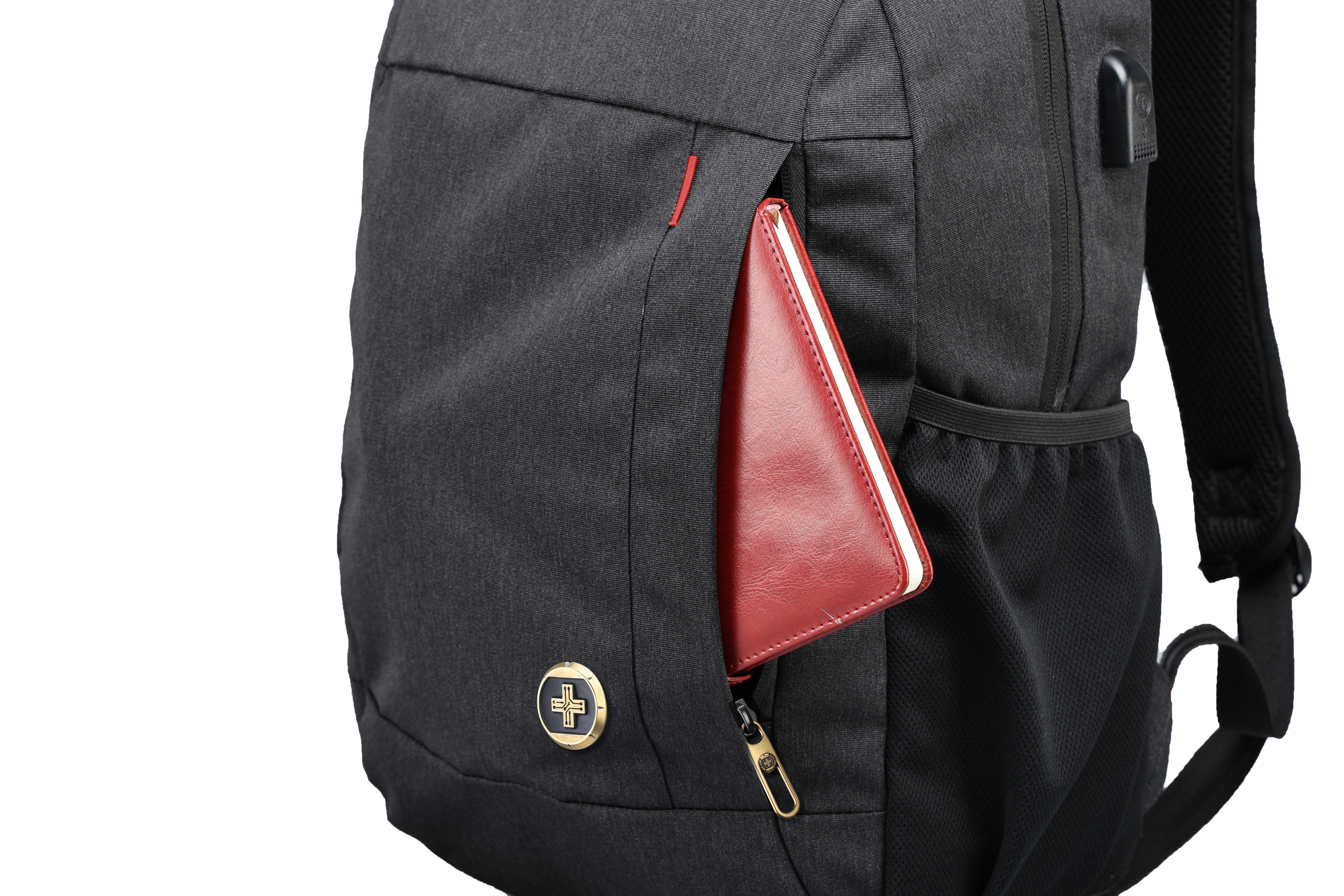Uno zaino nero con un taccuino rosso parzialmente visibile nella tasca anteriore. Visibile un'emblema dorato.