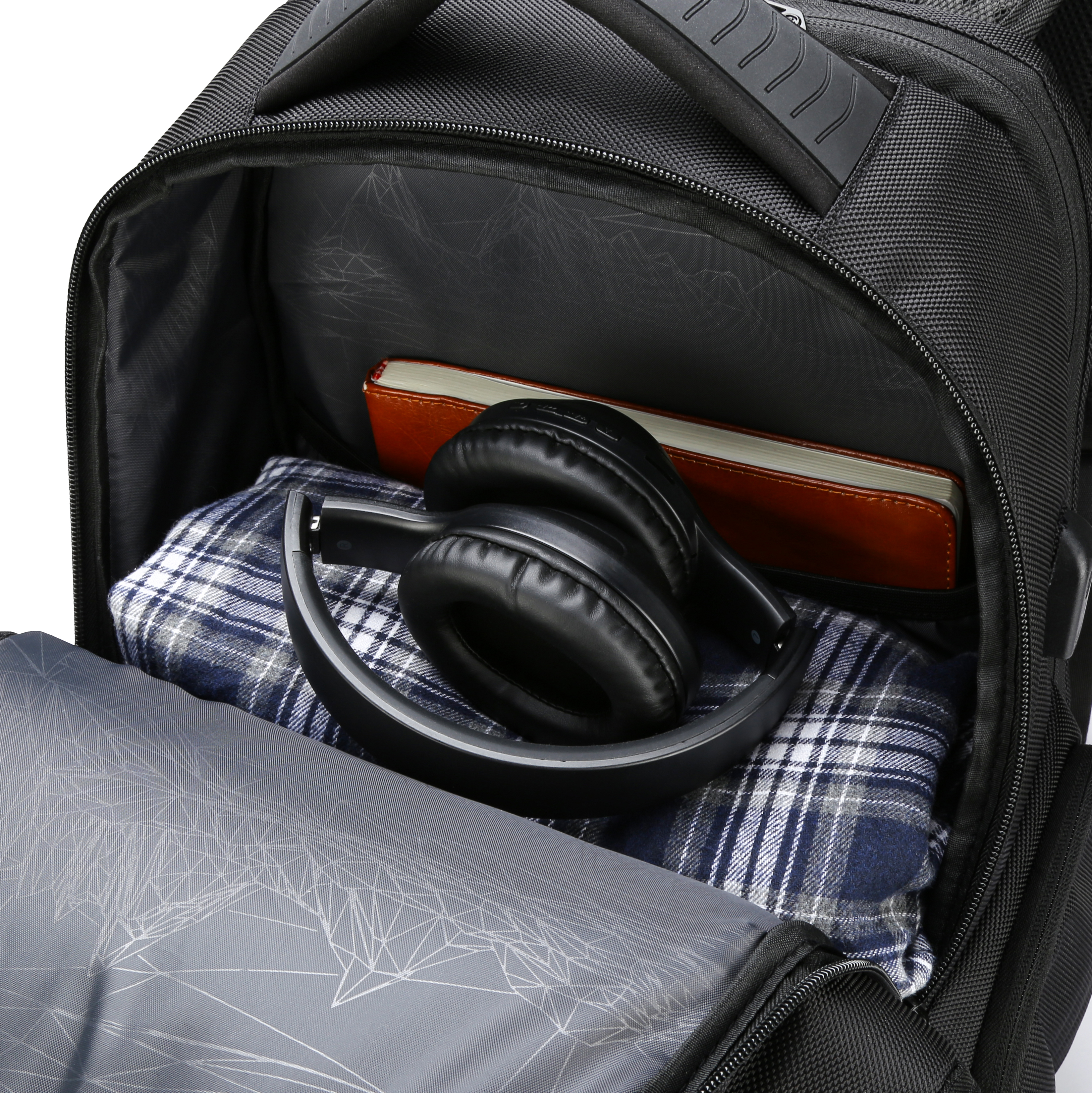 Zaino nero aperto, che rivela cuffie, camicia a quadri e quaderno marrone.