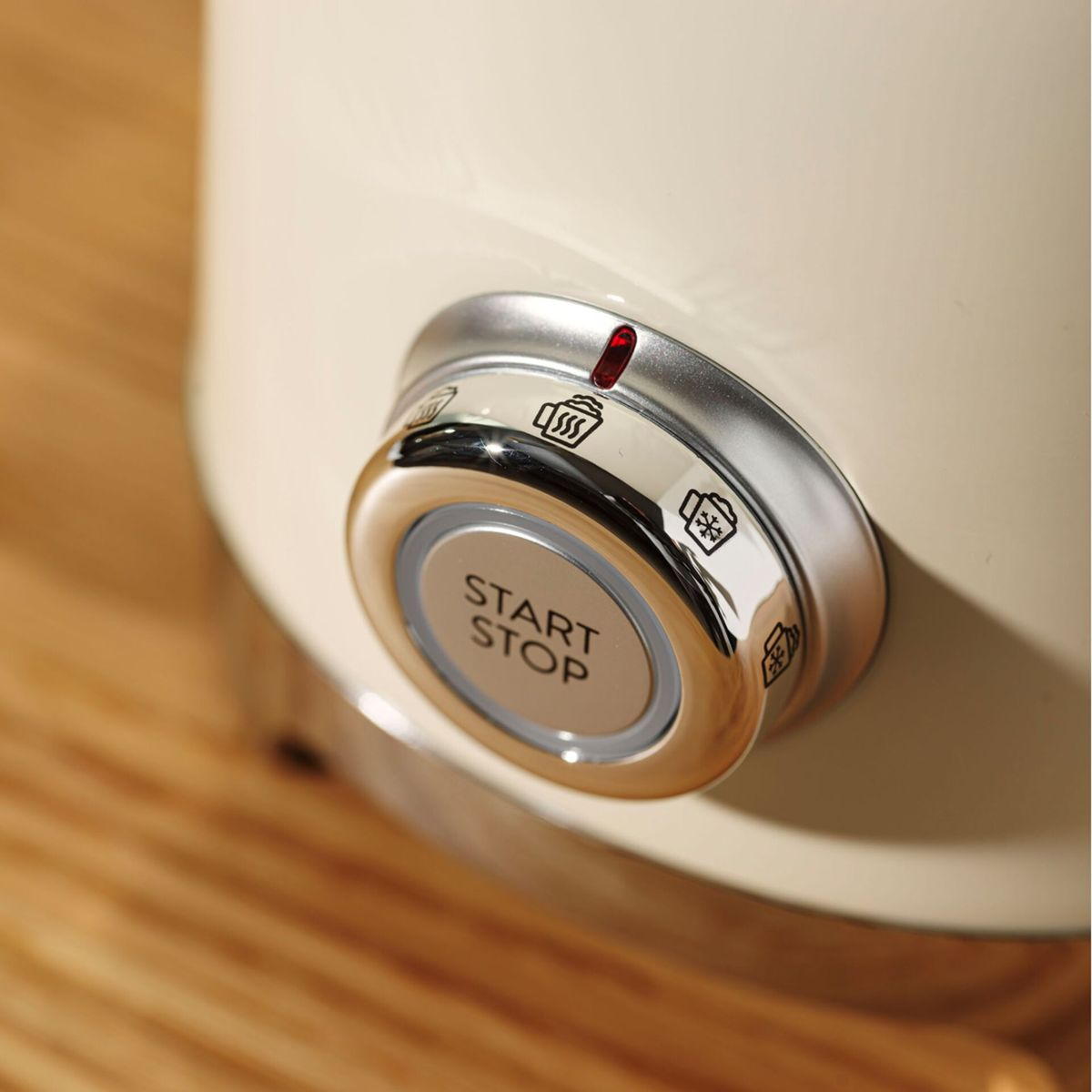 Zbliżenie kremowego pokrętła sterowania urządzenia z napisem 'START STOP'. Widoczne ikony i czerwone światło, na drewnie.