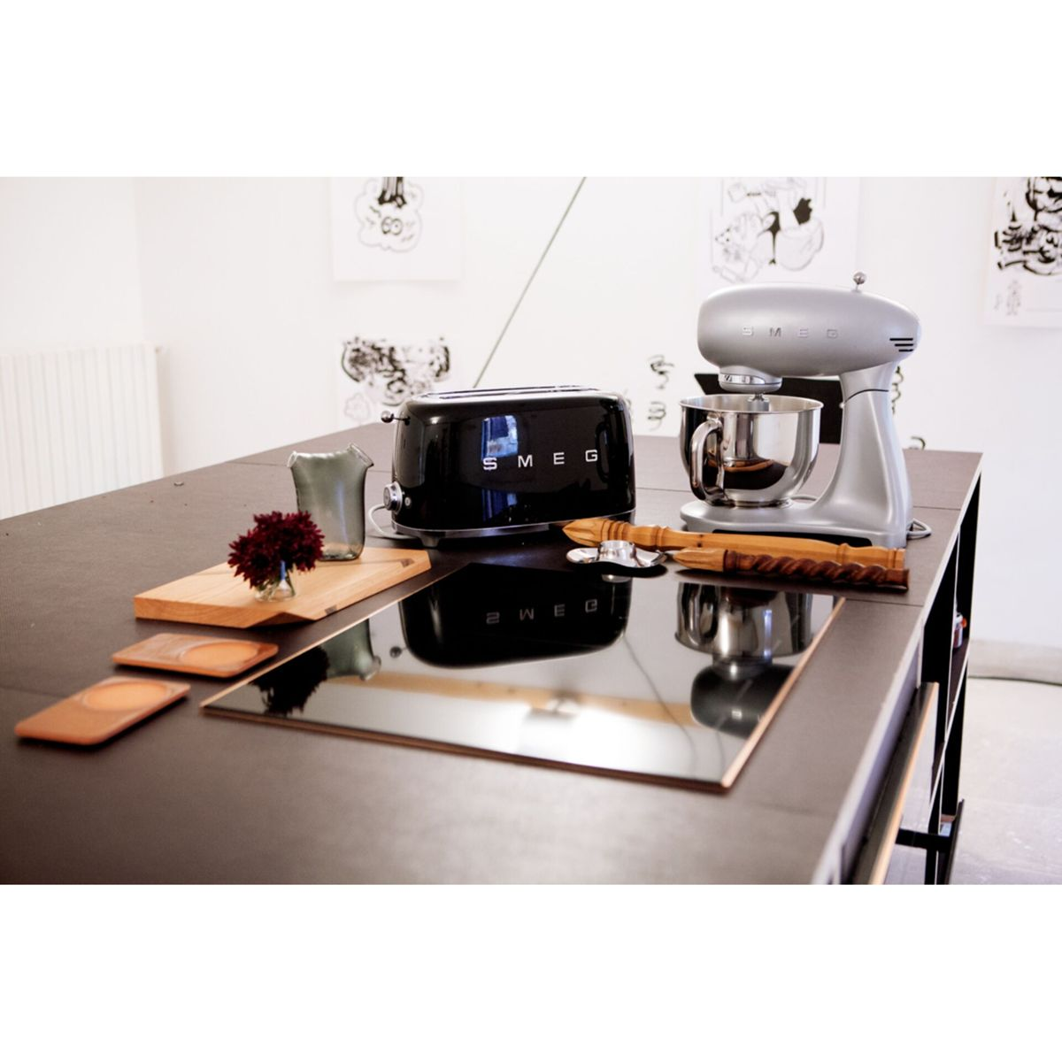 Blat kuchenny prezentuje czarny toster, srebrny mikser, drewniane przybory, wazon i deskę do krojenia z kwiatami.