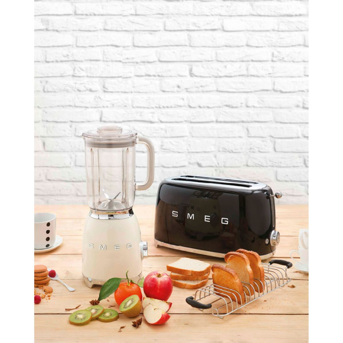 Scena kuchenna z blenderem, tosterem, owocami i chlebem na drewnianej powierzchni na tle białej ceglanej ściany.