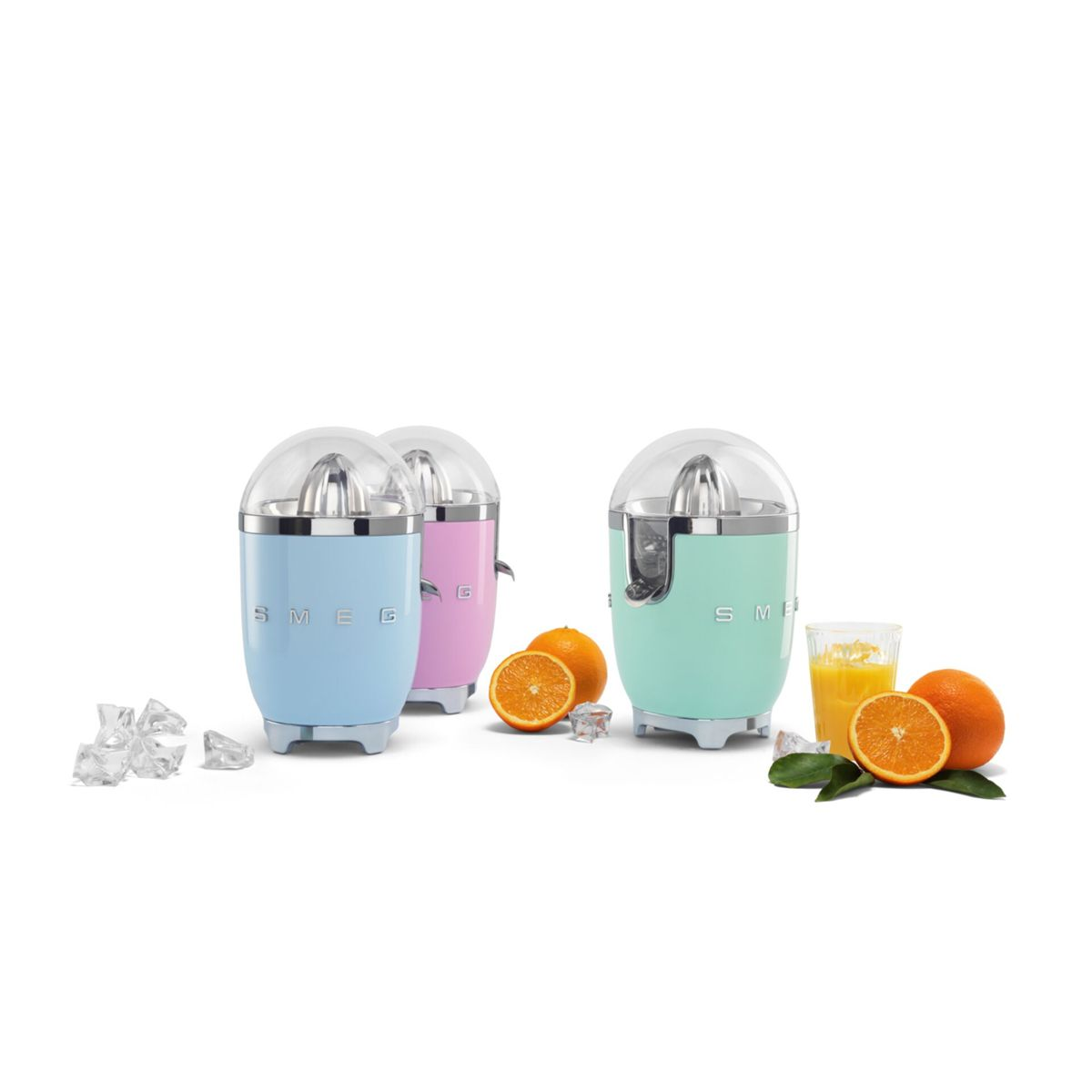 Trzy kolorowe wyciskarki do cytrusów, pomarańcze, kostki lodu i szklanka soku pomarańczowego na białej powierzchni. Wyciskarki są niebieskie, różowe i zielone.