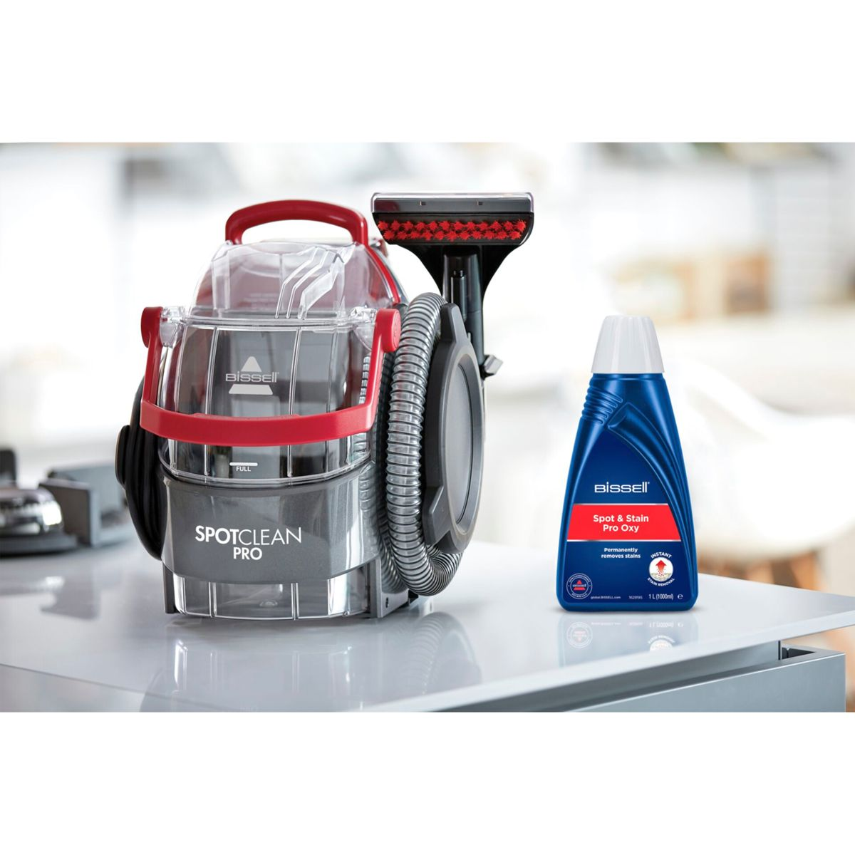 Een Bissell SpotClean Pro en een fles Spot & Stain Pro Oxy staan op een wit oppervlak. De reiniger is rood en grijs.