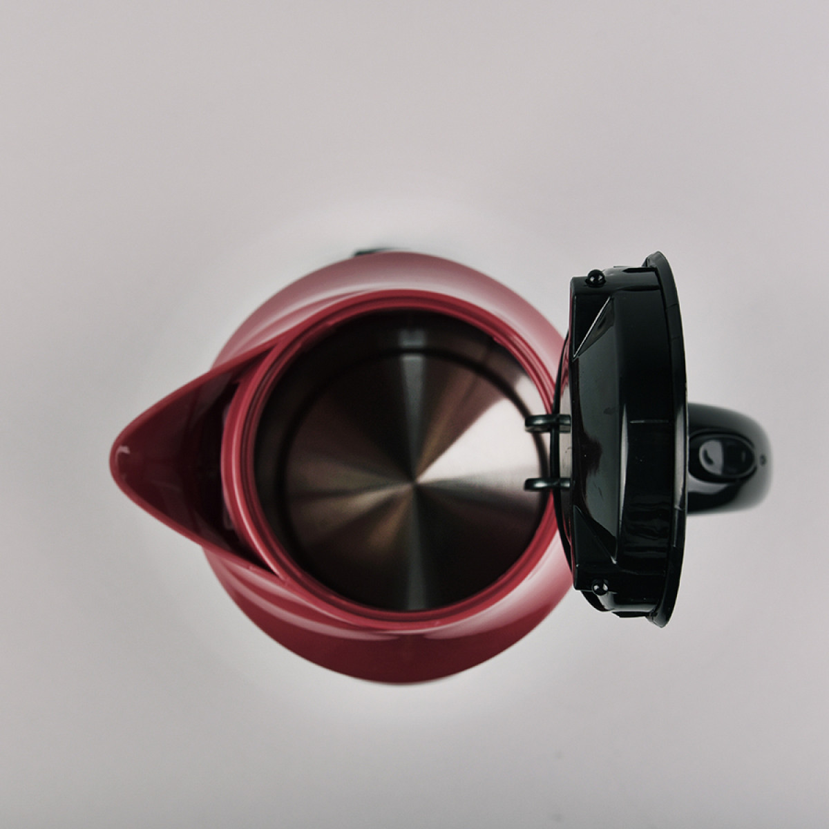 Widok z góry na czerwono-czarny czajnik elektryczny z otwartą pokrywą, na białym tle.