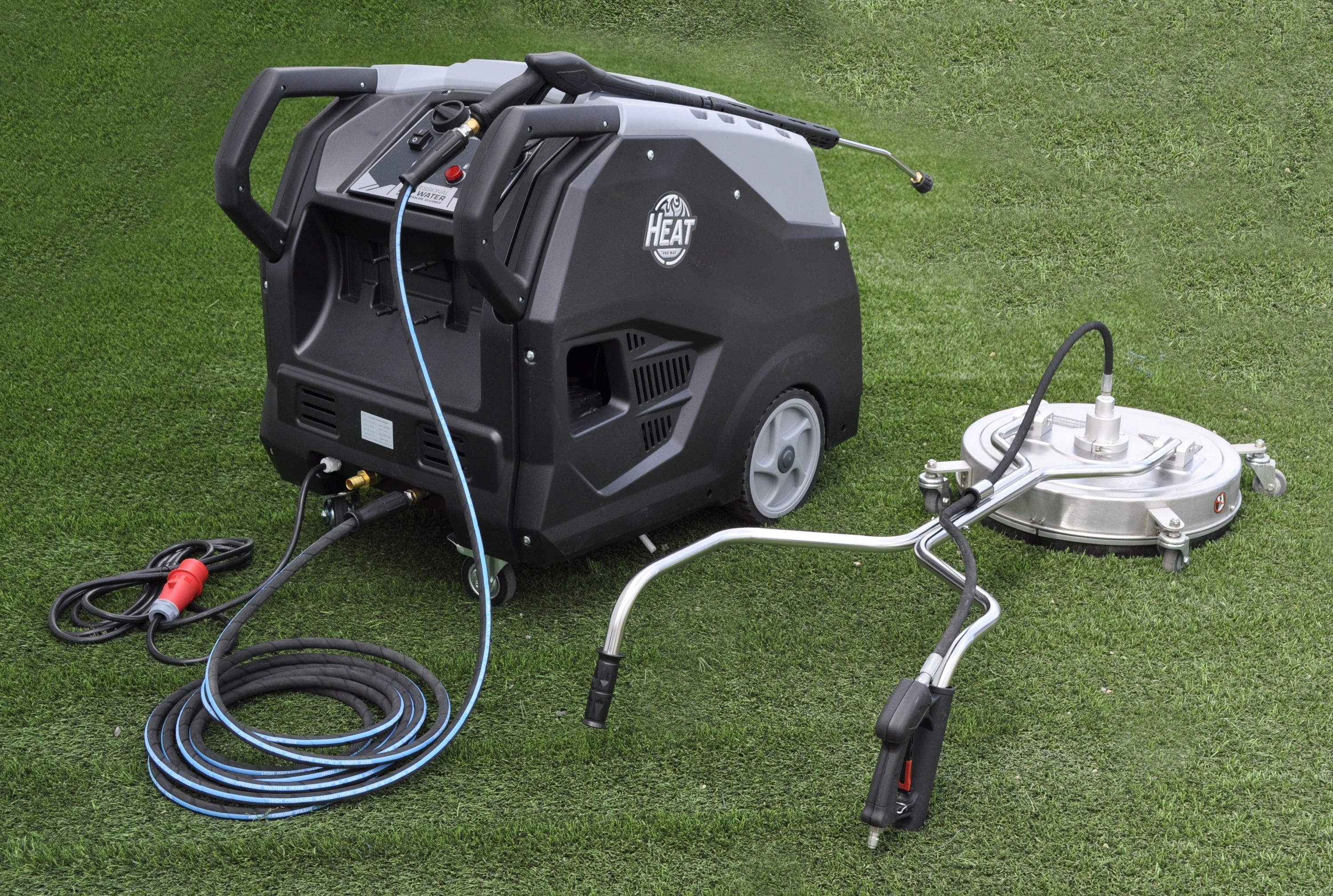 Ein schwarz-grauer Hochdruckreiniger mit Reinigungskopf auf grünem Gras. Kabel und Schläuche sind an die Maschine angeschlossen.