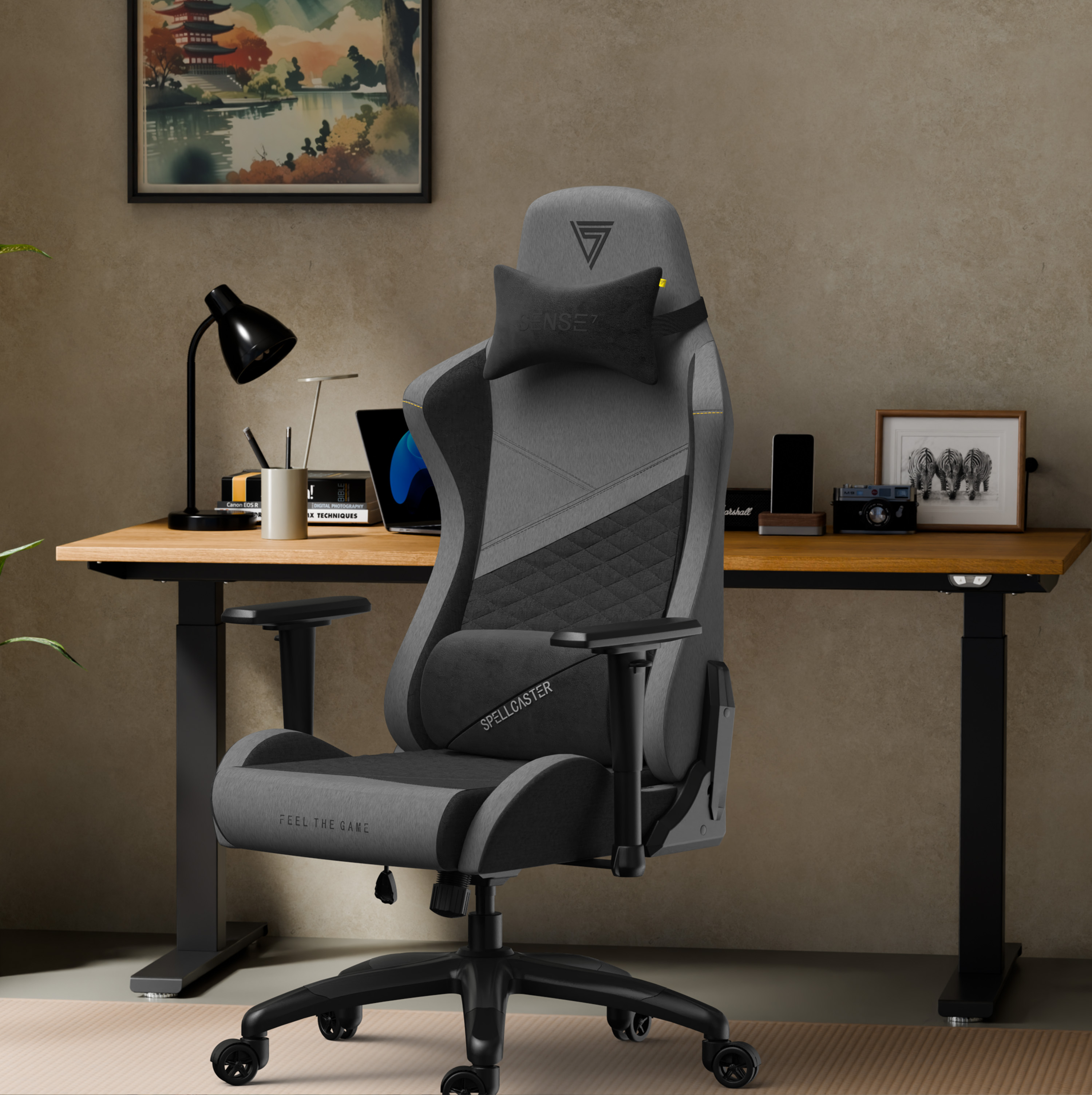 Een gamestoel staat voor een bureau met een laptop, lamp en kunstwerk. De stoel is grijs en zwart.