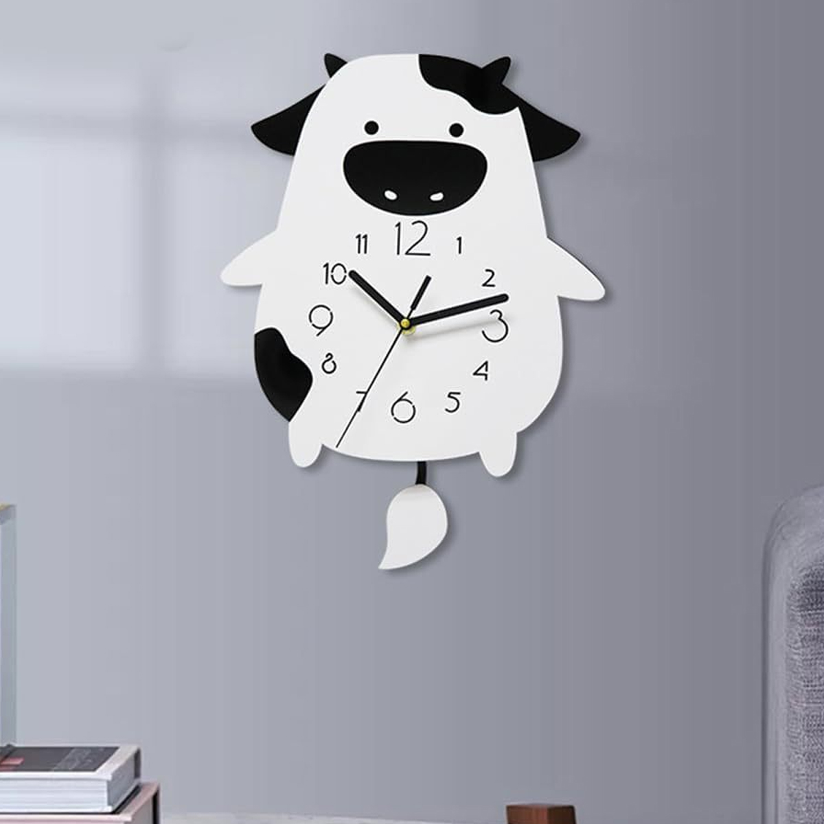 Eine kuhförmige Uhr mit schwarz-weißem Design hängt an einer grauen Wand. Die Uhr hat Zeiger, die auf 10 Minuten nach 12 zeigen.