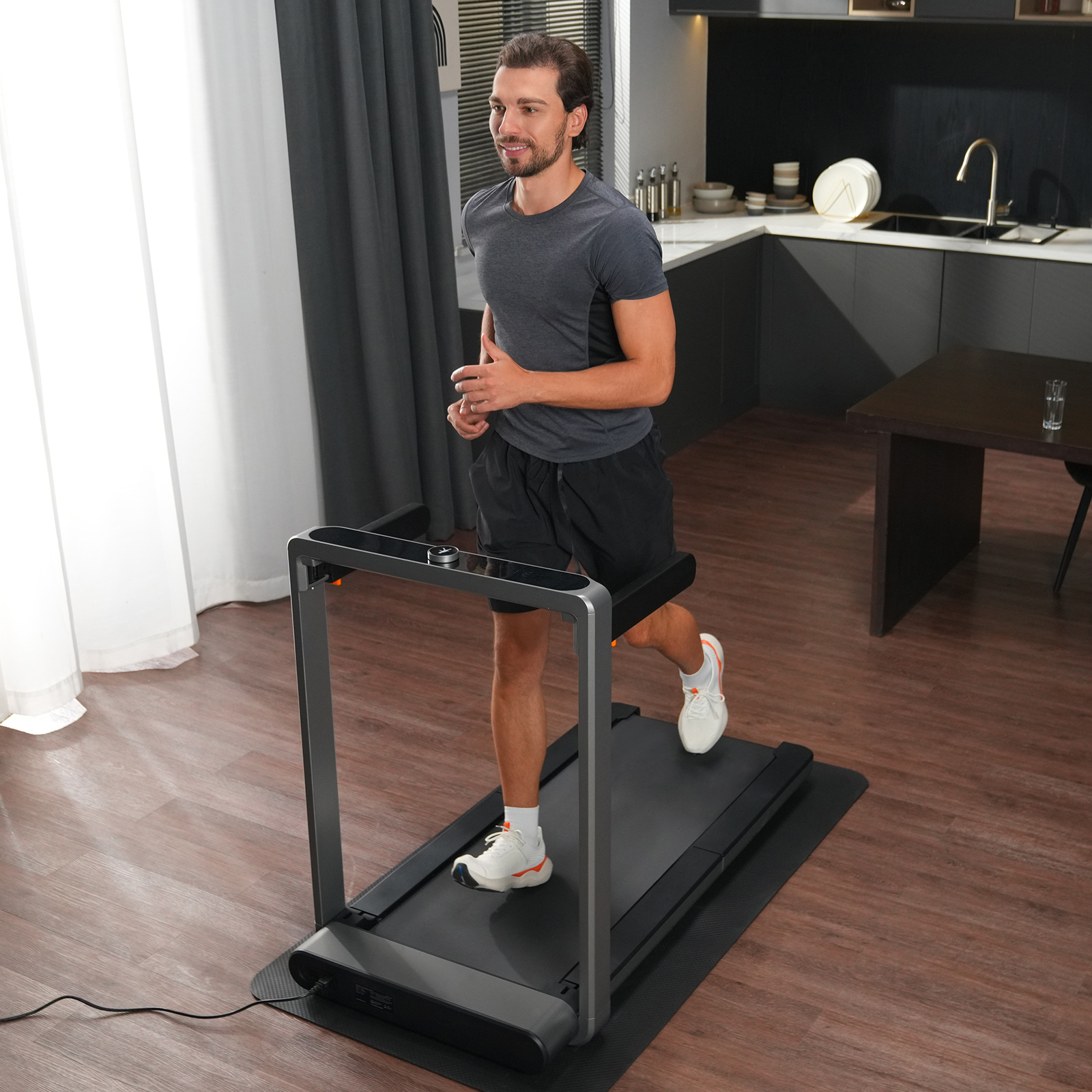 Ein Mann läuft drinnen auf einem Laufband. Er trägt Sportkleidung. Der Hintergrund zeigt eine Küche und einen Esstisch.