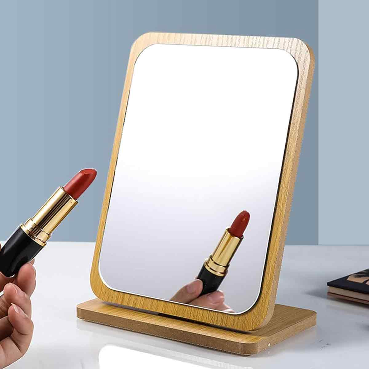 Ein Spiegel mit Holzrahmen und -sockel. Eine Hand hält roten Lippenstift. Der Spiegel reflektiert Lippenstift und Hand.