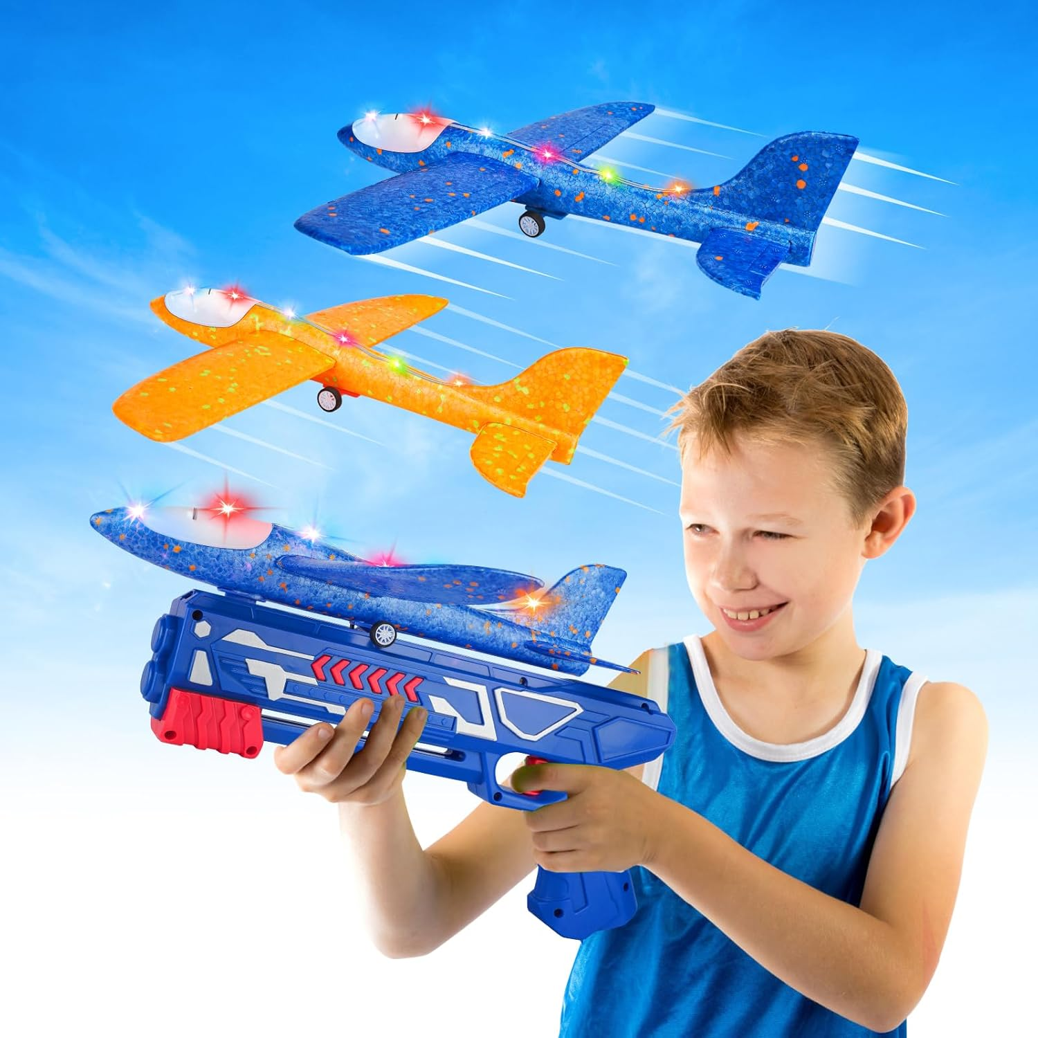 Ein Junge hält eine Spielzeugpistole, die Spielzeugflugzeuge abschießt. Drei Spielzeugflugzeuge sind am Himmel. Flugzeuge sind blau und orange.