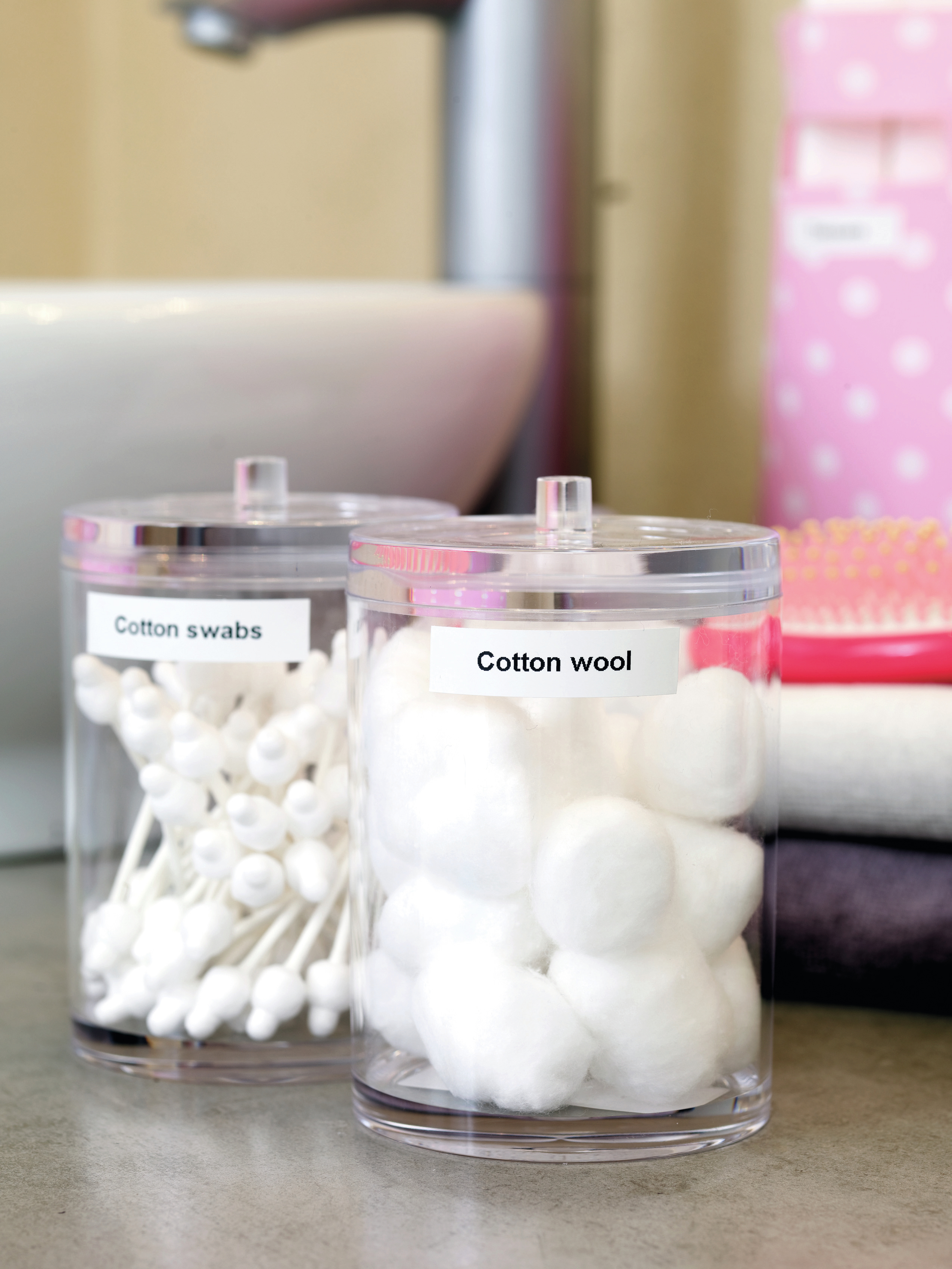 Dwa przezroczyste słoiki z pokrywkami, jeden z patyczkami do uszu, a drugi z watą, na blacie łazienkowym.