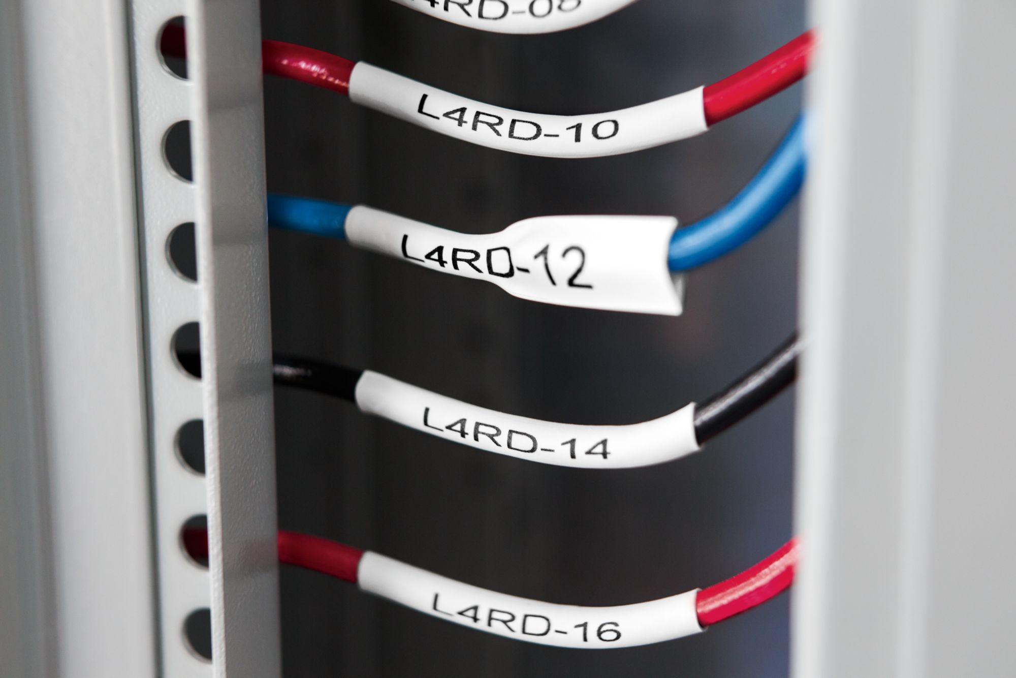 Close-up of labeled wires. Red, blue, and black wires are visible, each with a white label marked with L4RD and numbers. A metal frame is on the left.