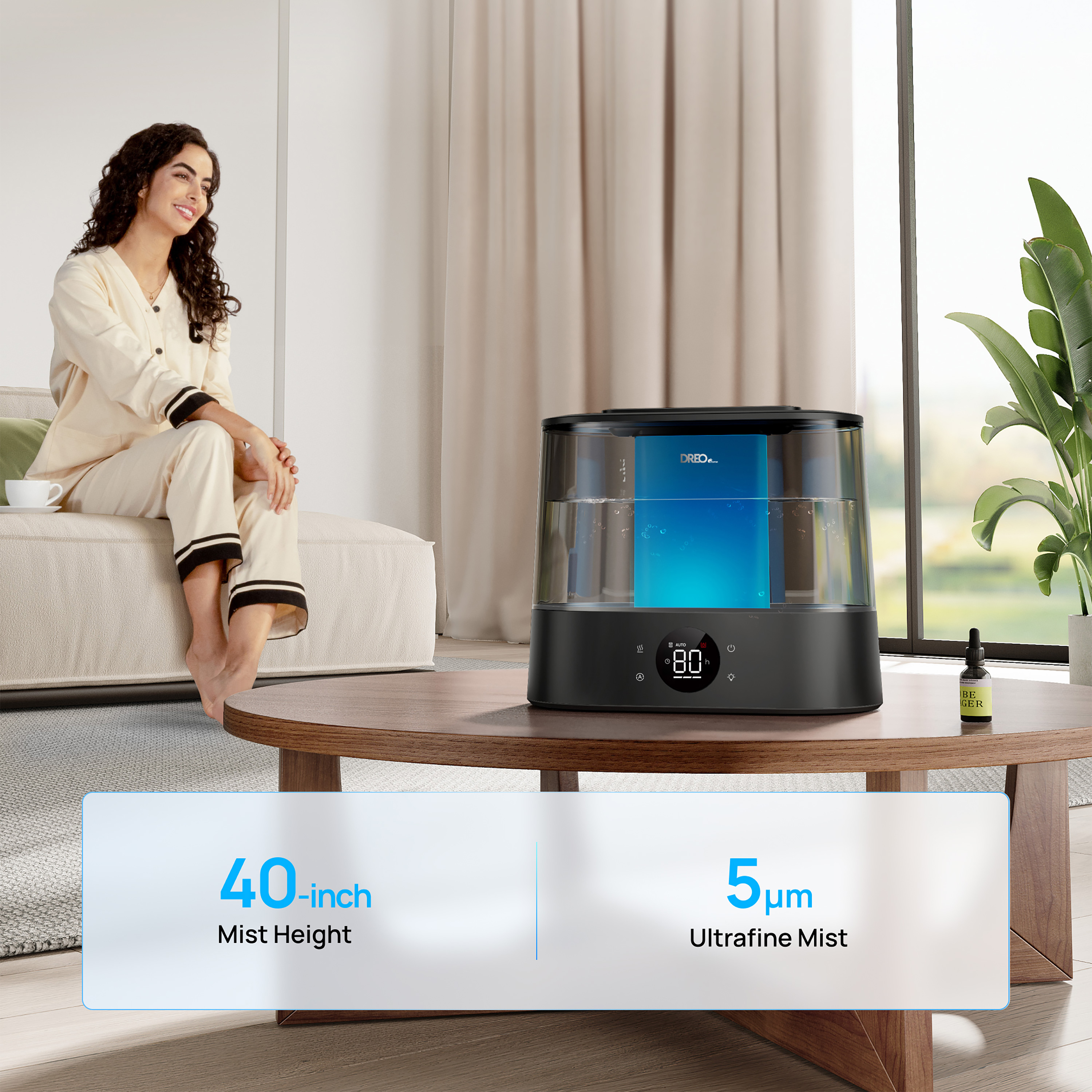 Una mujer está sentada cerca de un humidificador en una mesa. El humidificador tiene una pantalla que muestra 80.