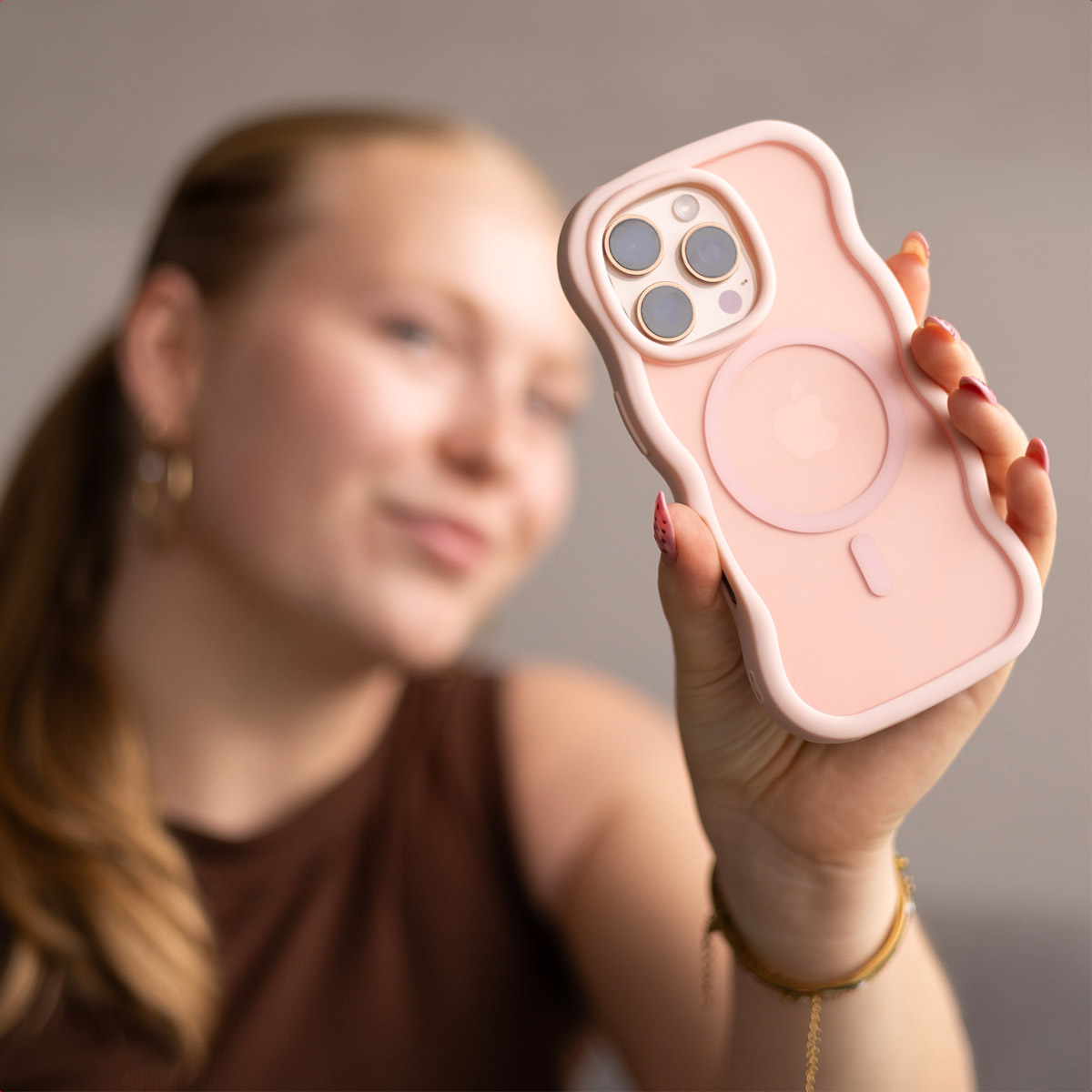 Eine Frau hält eine rosa Handyhülle hoch. Die Hülle ist im Fokus, die Frau ist unscharf. Die Handyhülle hat einen MagSafe-Kreis.