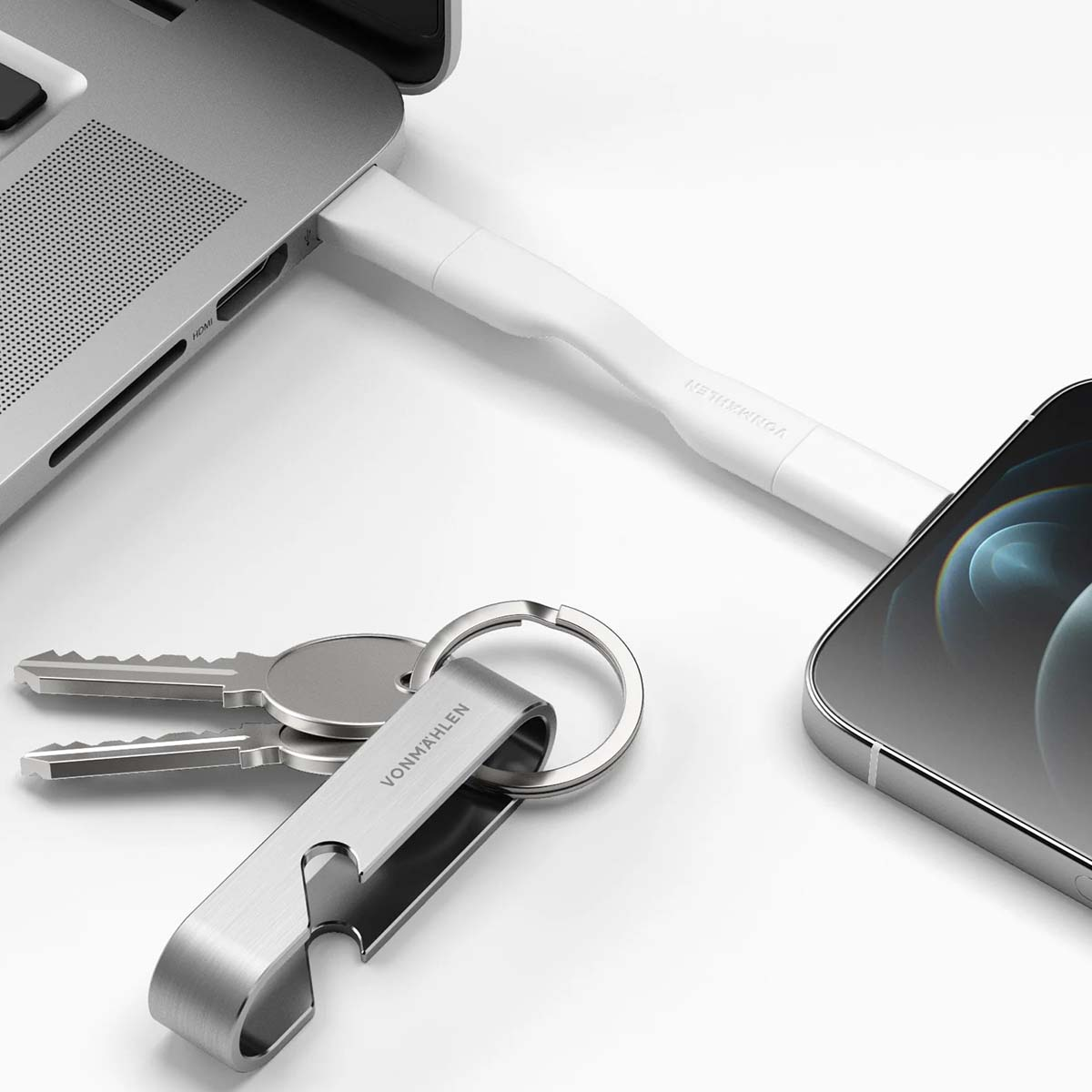 Ordinateur portable, téléphone, clés et chargeur sur surface blanche. Le chargeur est connecté à l'ordinateur et au téléphone.