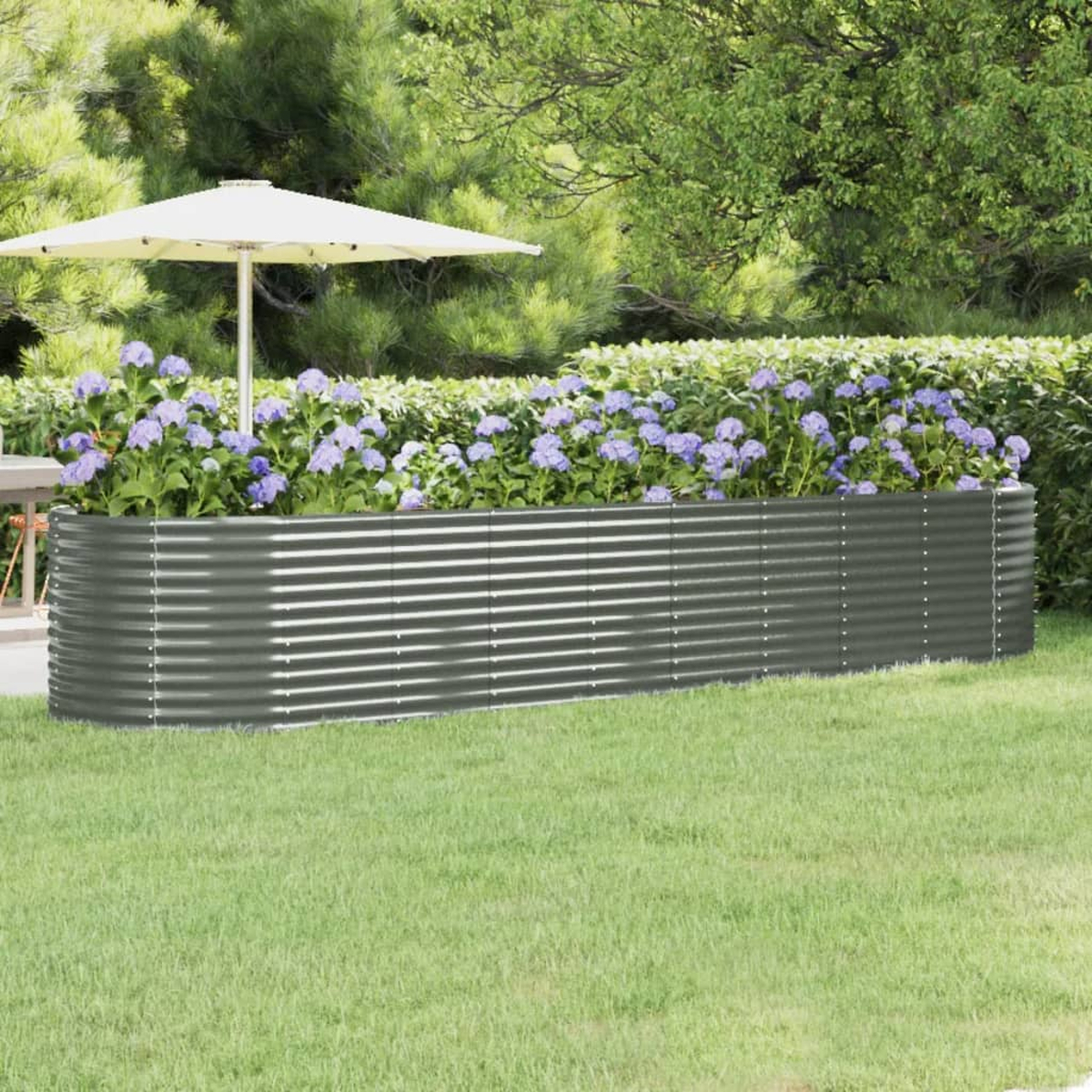 Ein erhöhtes Gartenbeet aus Metall mit blauen Blumen, einem weißen Sonnenschirm und grünem Gras und Bäumen im Hintergrund.