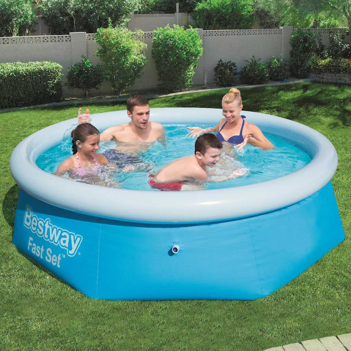 Familie in einem aufblasbaren Pool. Zwei Erwachsene und zwei Kinder sind im Wasser. Blauer Pool auf grünem Gras. Bäume und Zaun im Hintergrund.
