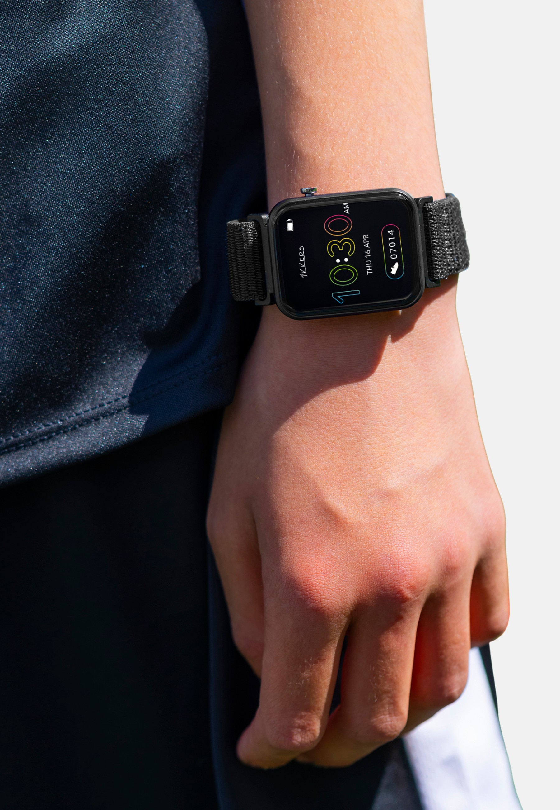 Das Handgelenk einer Person mit einer schwarzen Smartwatch, die 10:30 Uhr anzeigt. Die Uhr hat ein schwarzes Armband. Die Person trägt dunkle Kleidung.