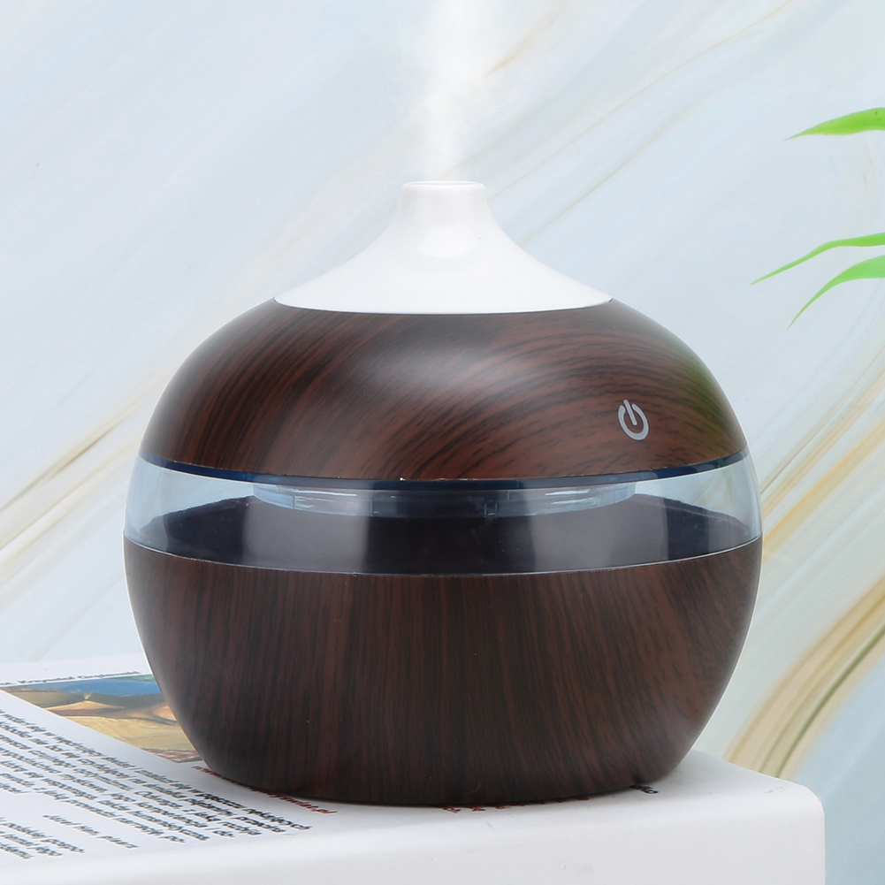Ein holzstrukturiertes ätherisches Öl Diffusor mit weißer Oberseite, klarem Mittelteil und Power-Taste. Dampf steigt auf.