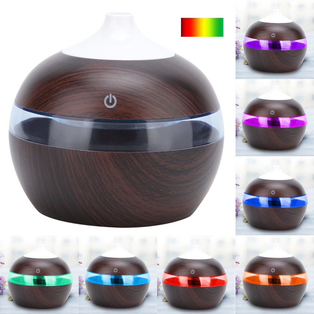 Ein Aromatherapie-Diffusor mit Holzmaserung. Er hat einen weißen Deckel und einen Ring aus farbigem Licht. Mehrere Diffusoren werden mit verschiedenen Lichtfarben gezeigt.