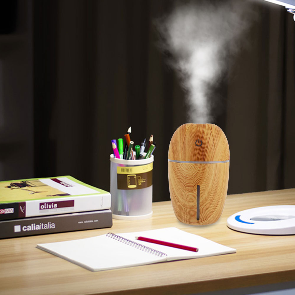 Ein Holz-Luftbefeuchter auf einem Schreibtisch. Ein Notizbuch, Bleistifte und Bücher liegen ebenfalls auf dem Tisch. Dampf steigt auf.