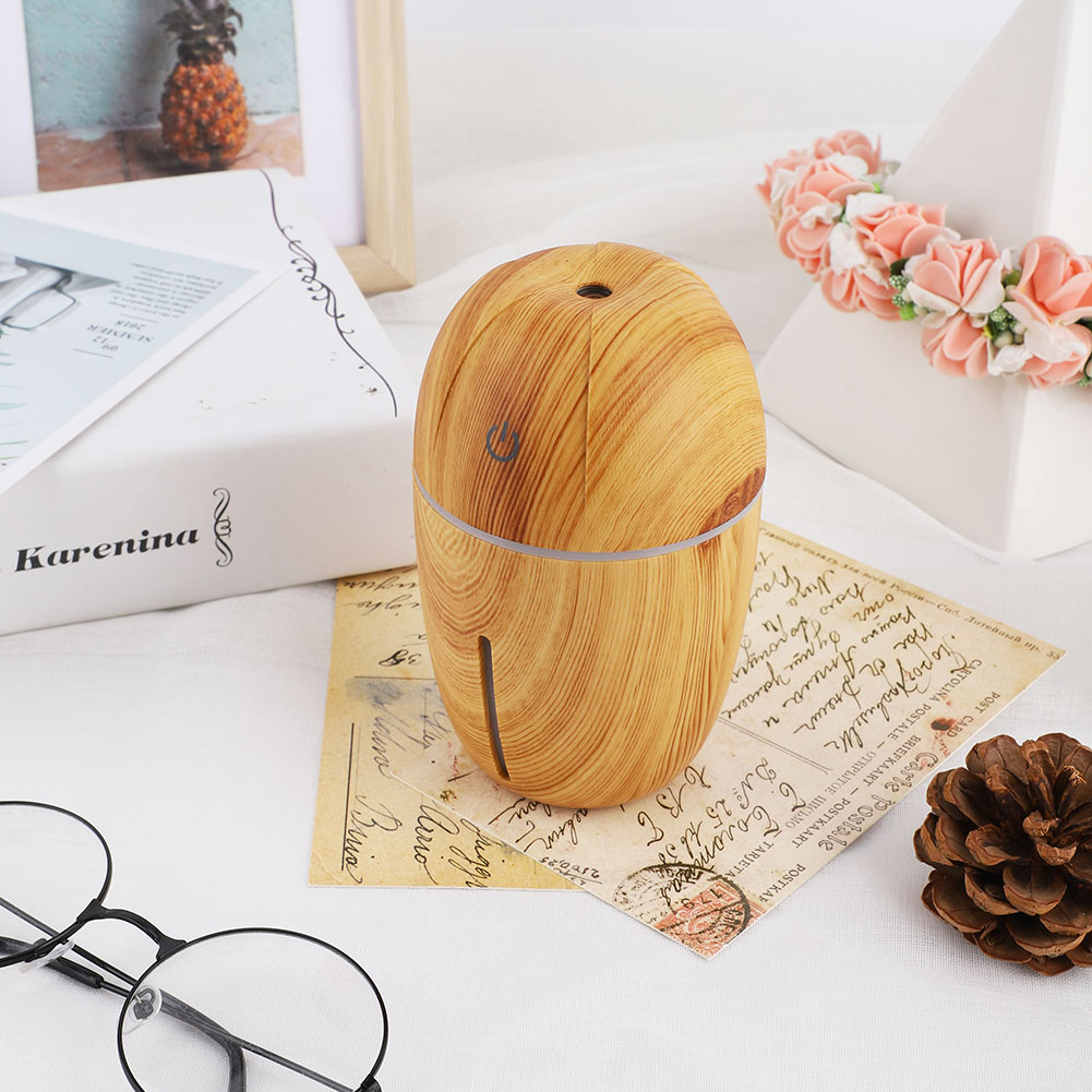 Ein Holz-Look-Diffusor für ätherische Öle. Daneben sind ein Buch, eine Brille, dekorative Gegenstände und ein Tannenzapfen zu sehen.
