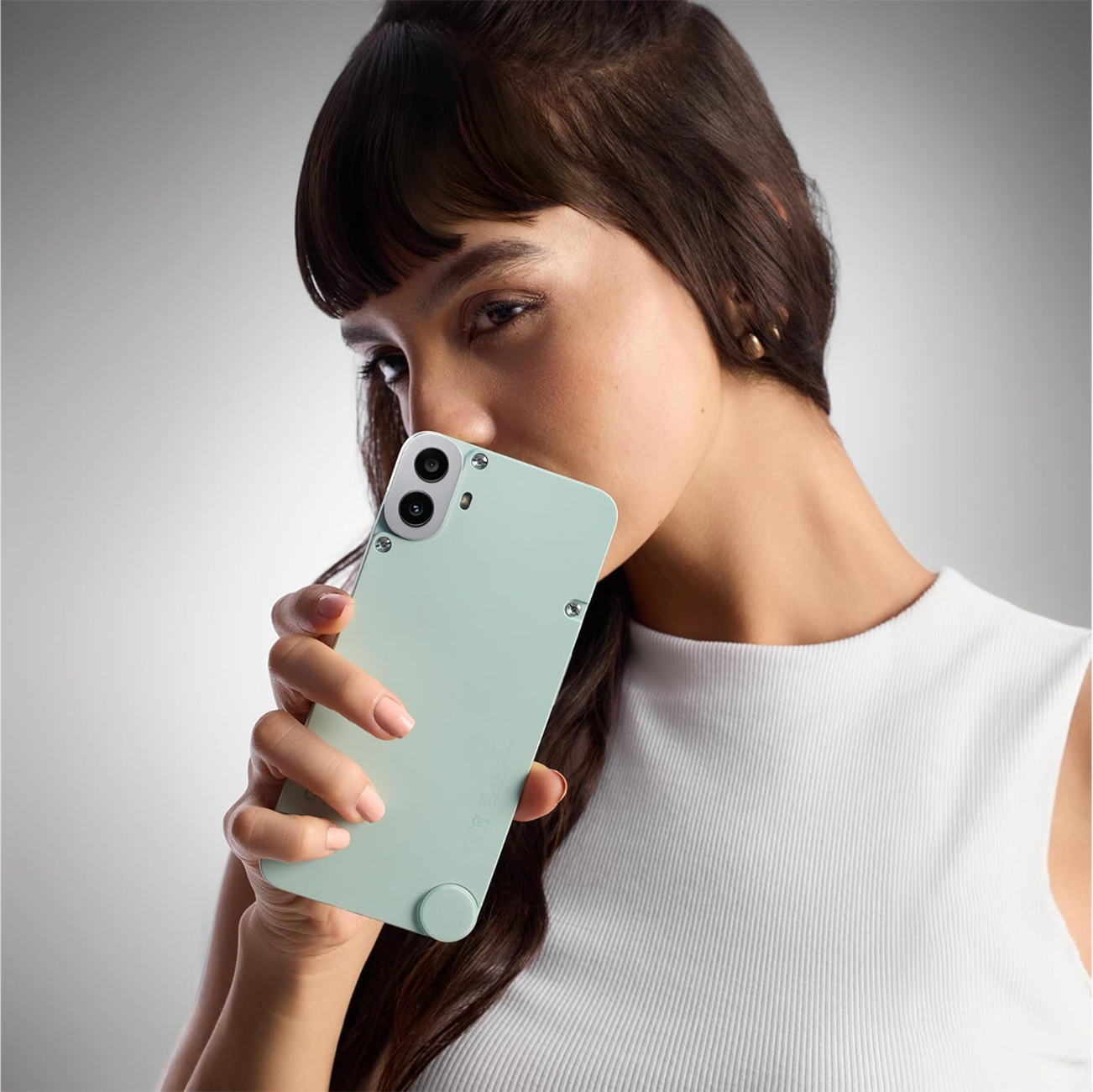 Eine Frau hält ein mintgrünes Telefon nah an ihrem Gesicht. Sie trägt ein weißes Oberteil. Das Telefon hat zwei Kameras.