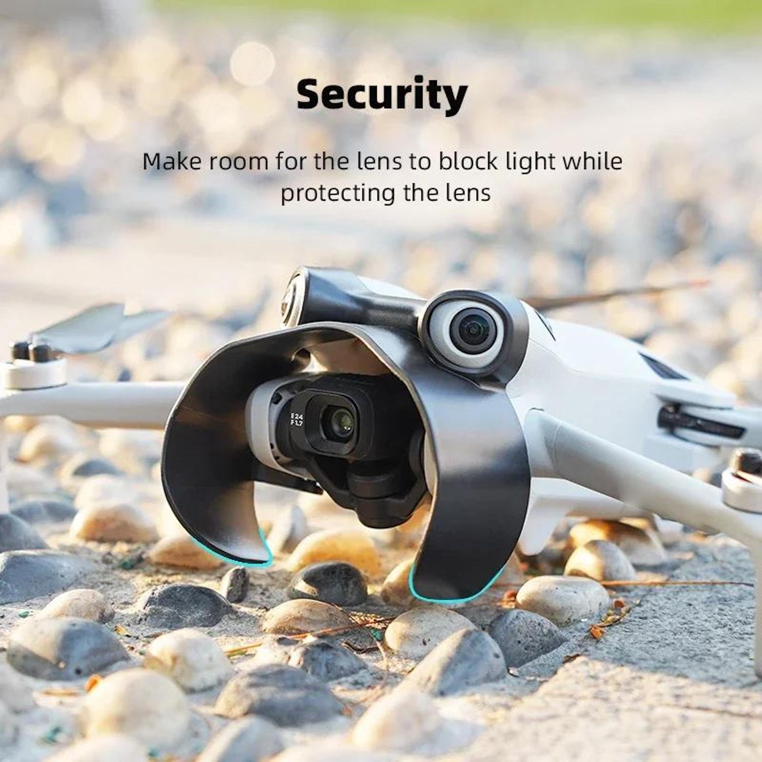 Un drone bianco con protezione dell'obiettivo su una superficie sabbiosa con piccole pietre. Testo: Sicurezza, Fai spazio all'obiettivo.