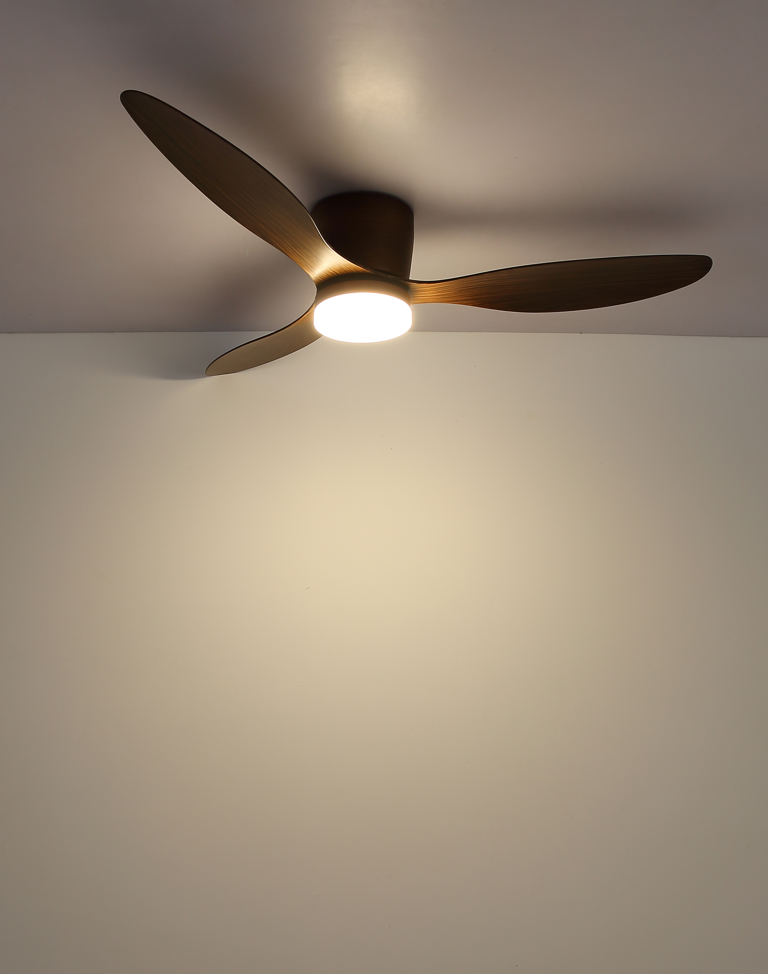 Ein Deckenventilator mit drei Flügeln und einem zentralen Licht. Der Hintergrund ist eine weiße Wand.