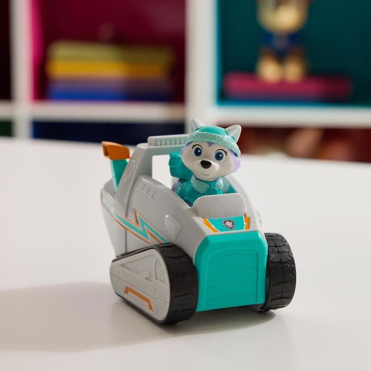 Ein Spielzeugfahrzeug mit einer Zeichentrickfigur am Steuer. Das Fahrzeug ist weiß und türkis mit schwarzen Ketten. Die Figur ist ein weißer Hund.