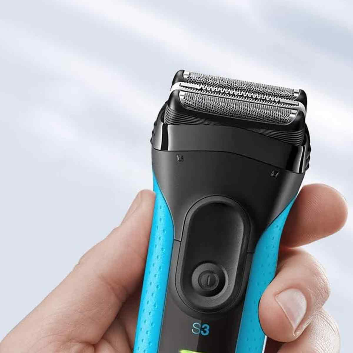Ein blau-schwarzer Elektrorasierer wird in einer Hand gehalten. Der Rasiererkopf ist silbern. Der Hintergrund ist ein verschwommenes Hellblau.