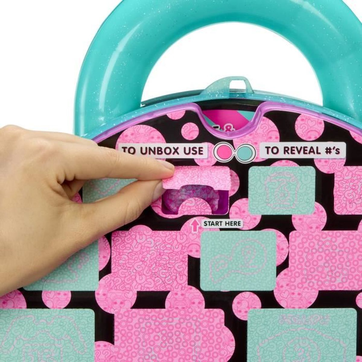 Eine Hand, die eine pinkfarbene Klappe mit der Aufschrift 'to unbox use' von einer Spielzeugkiste abzieht. Die Kiste ist mit rosa und tealfarbenen Mustern verziert.