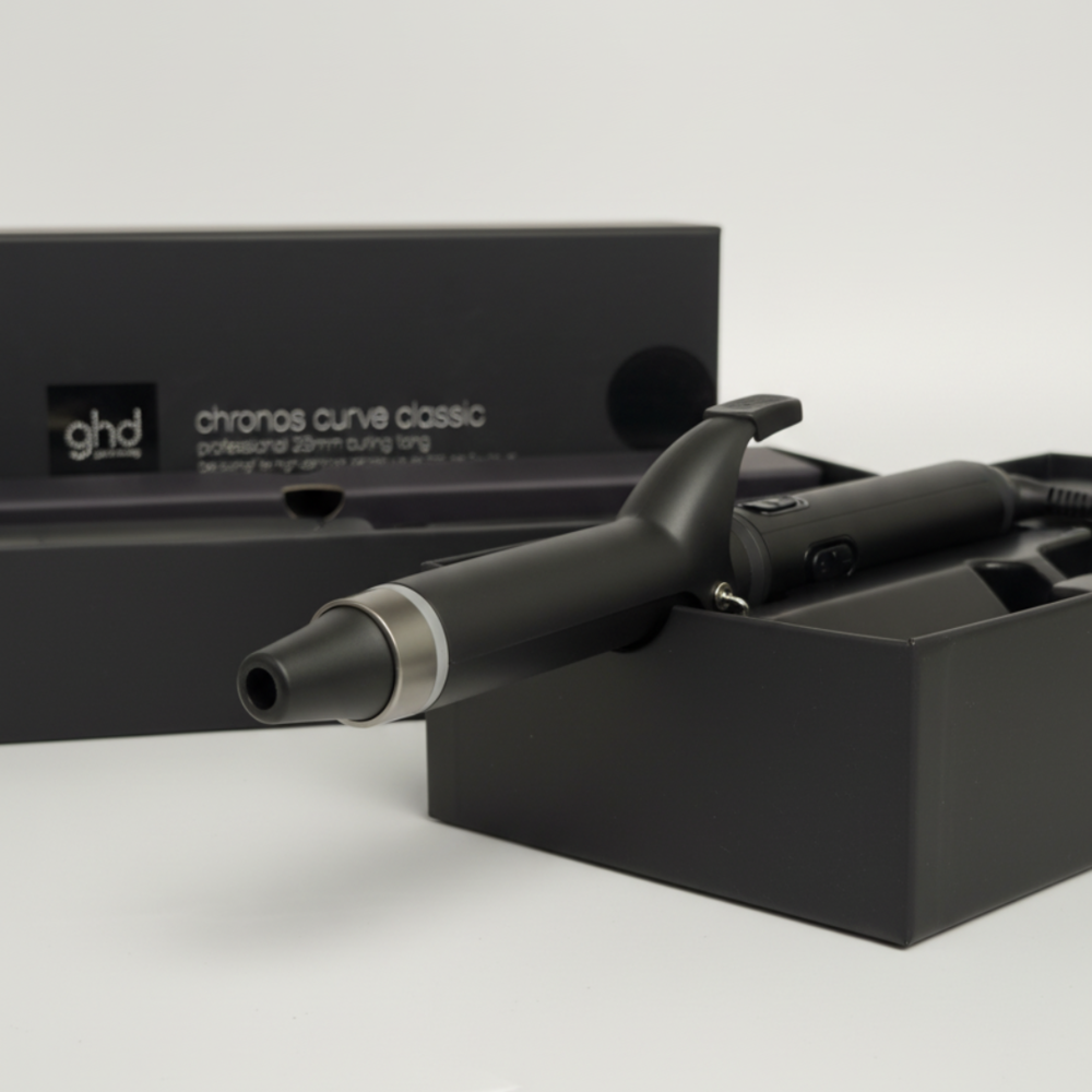 Un arricciacapelli GHD Chronos Curve Classic nero nella sua scatola. La scatola è nera con testo bianco. Lo sfondo è bianco.