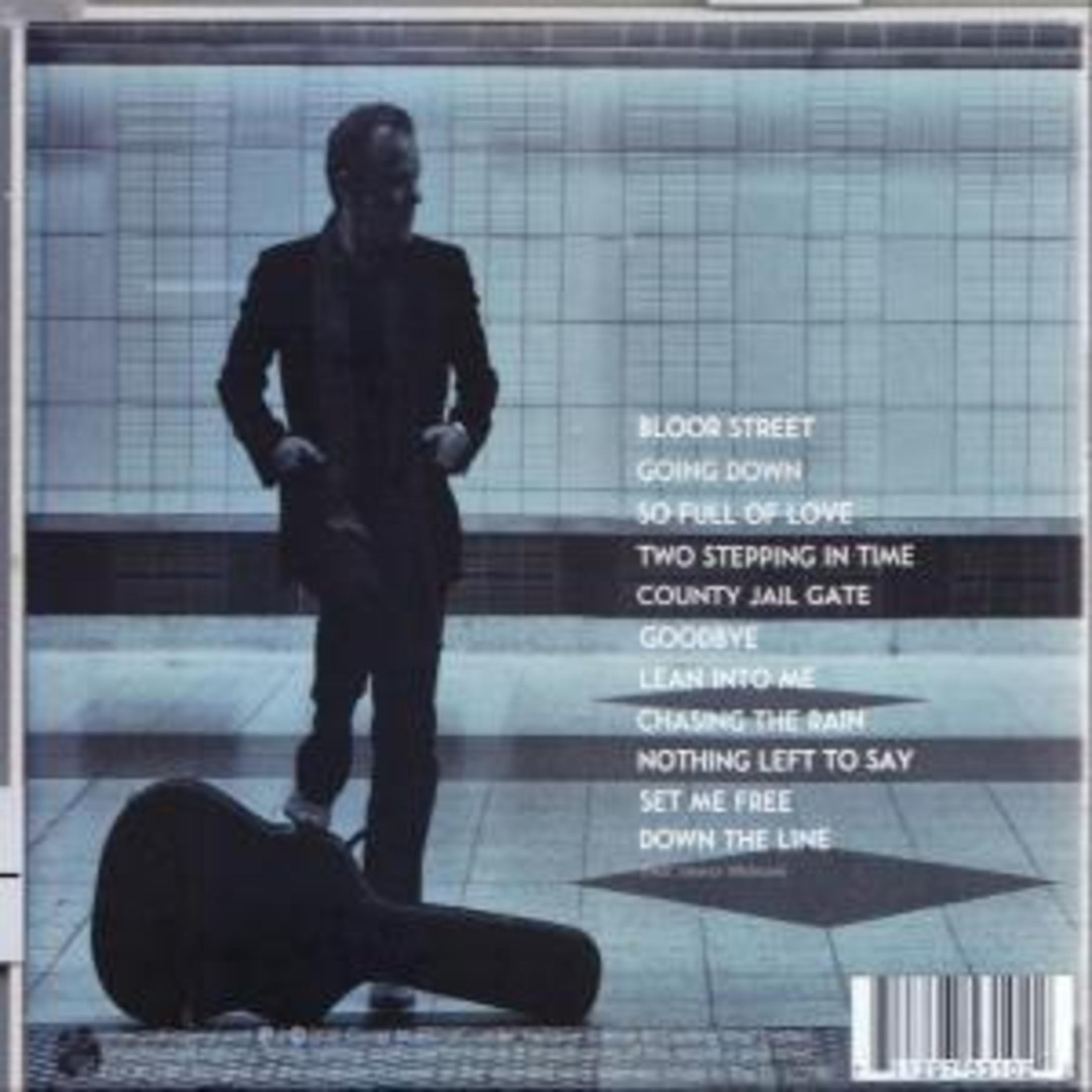 Ein Mann im Anzug steht neben einem Gitarrenkoffer. Albumtracks sind auf blauem Hintergrund gelistet.