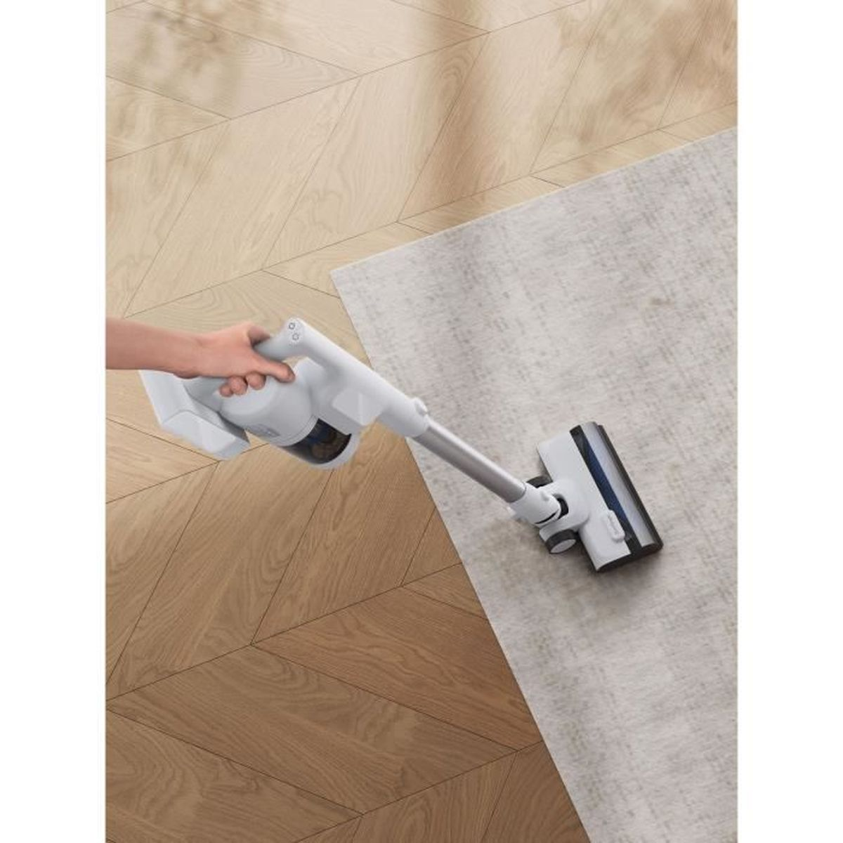 Une personne passe l'aspirateur sur un tapis clair avec un aspirateur blanc et argent sur un plancher de bois.