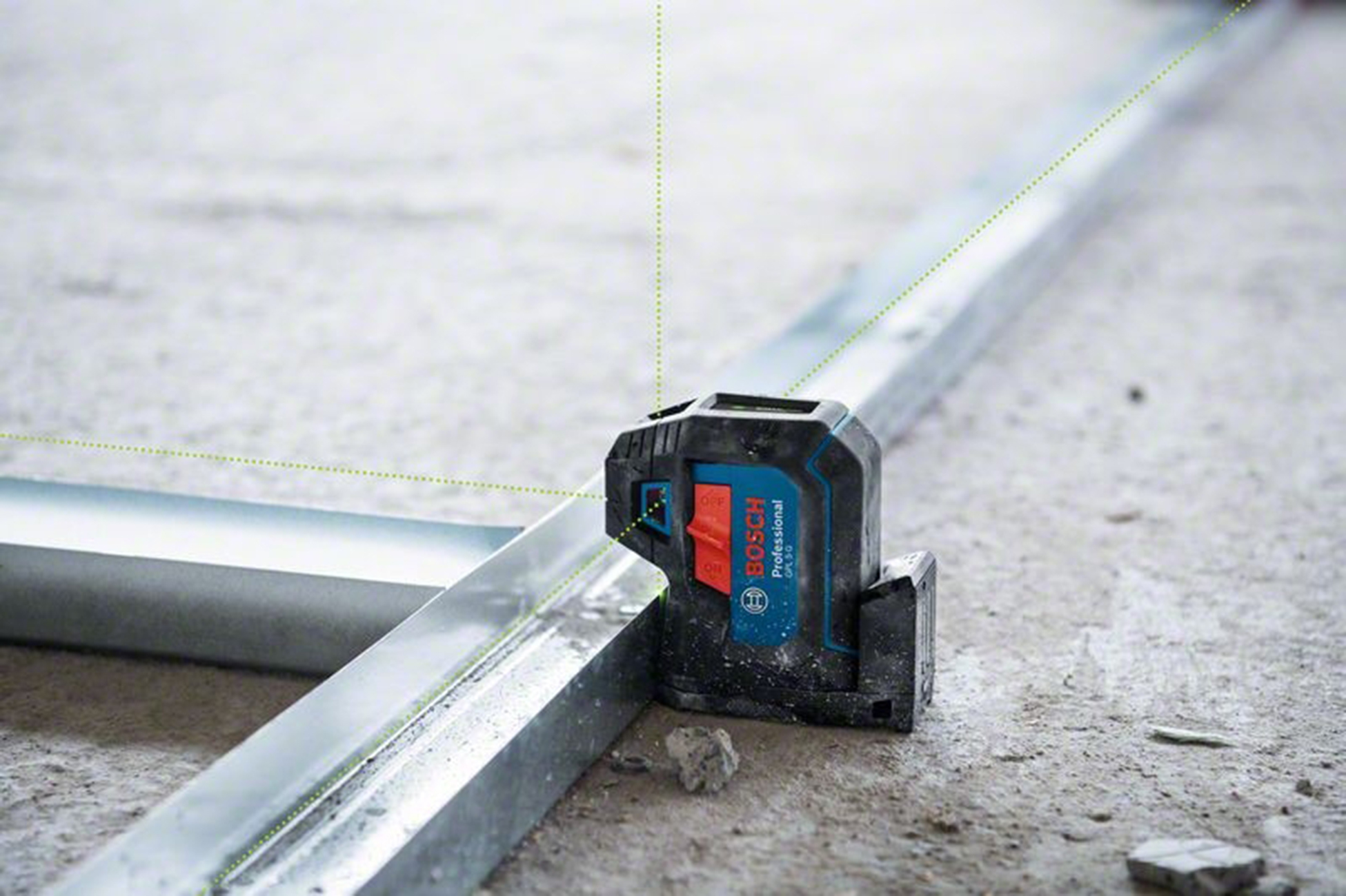 Bir Bosch lazer terazisi, metal kirişlere yeşil çizgiler yansıtır. Cihaz siyah ve mavidir, kırmızı bir düğmesi vardır. Yüzey betondur.