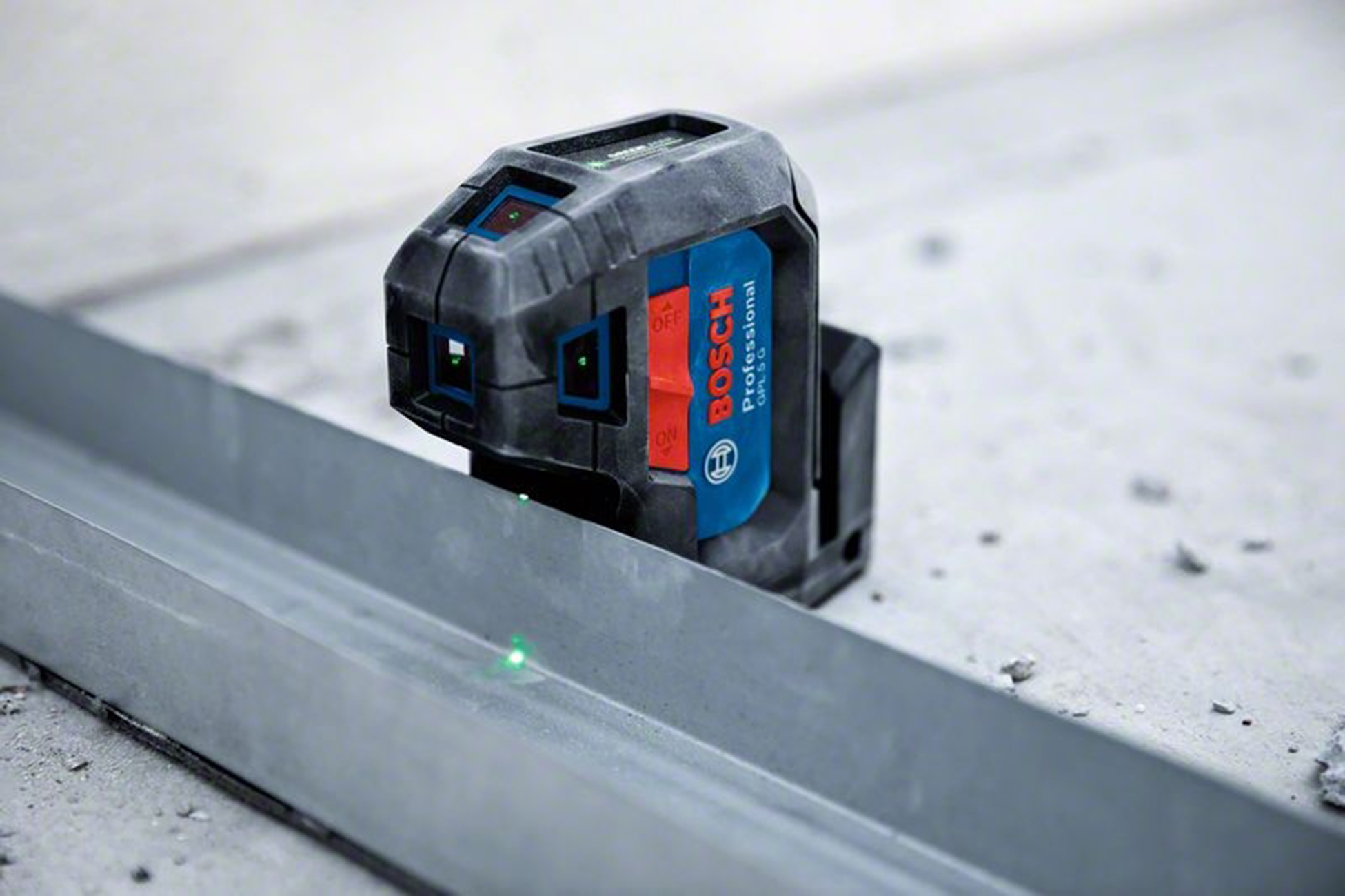 Bir Bosch lazer terazisi, metal bir kanala yeşil bir çizgi yansıtır. Alet siyah ve mavidir, beton bir yüzeyde duruyor.