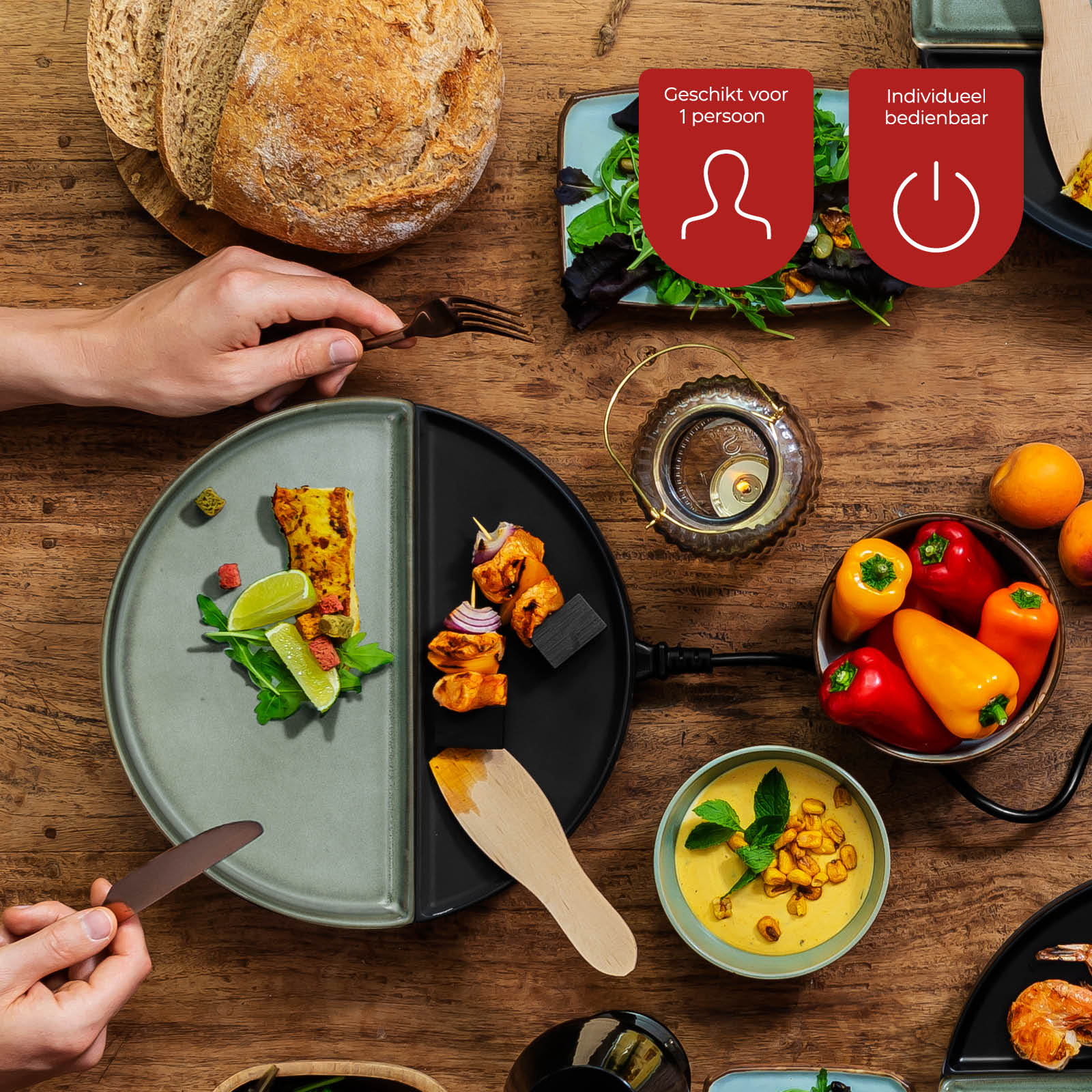 Overhead shot of a wooden table set for a meal. Includes bread, plates of food, peppers, soup, and hands holding cutlery.