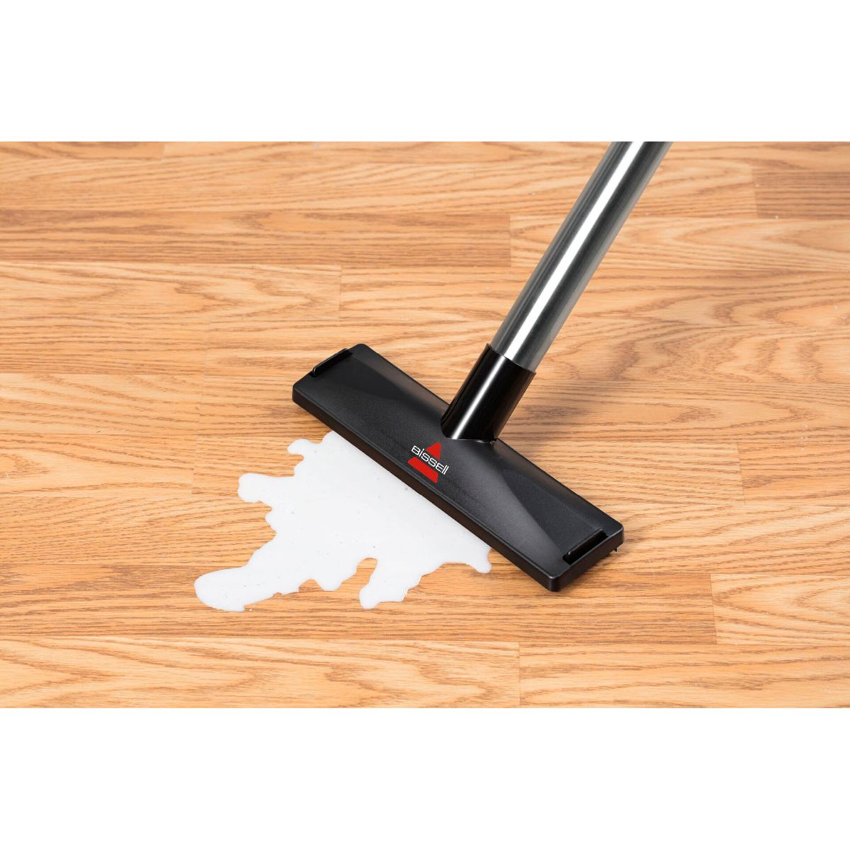 Een zwarte Bissell stofzuigerkop maakt een witte vlek schoon op een houten vloer. De stofzuiger heeft een zilveren handvat.