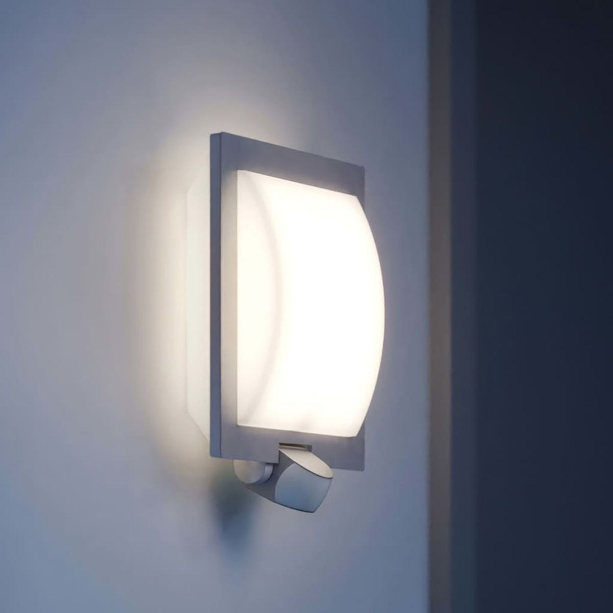 Eine moderne Wandlampe mit hellem, geschwungenem Lichtpaneel. Sie ist an einer hellblauen Wand montiert, rechts ein dunkelblauer Wandabschnitt.