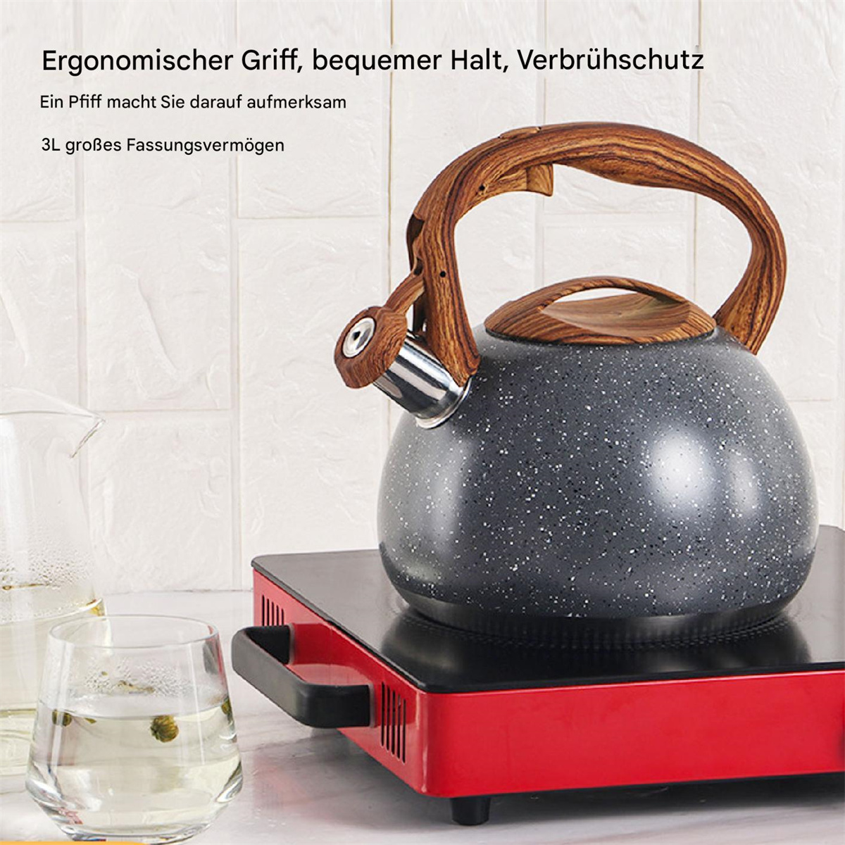 Ein schwarzer, gesprenkelter Wasserkocher mit Holzgriff auf einem roten Herd. Ein Glas Wasser mit Blumen und ein Glasbehälter links.