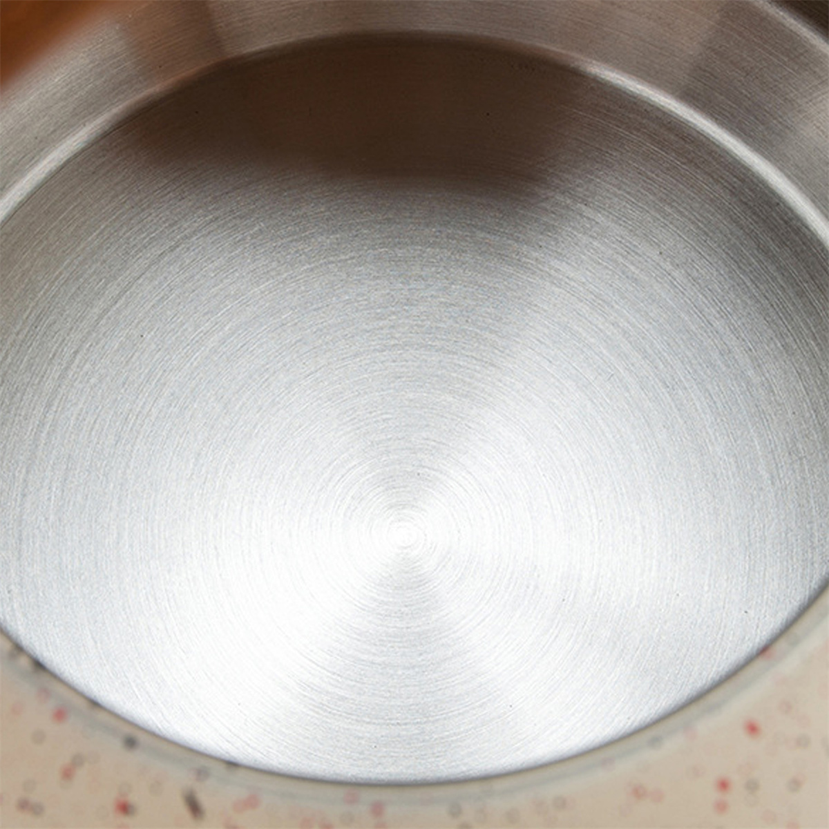 Nahaufnahme einer gebürsteten Metalloberfläche mit kreisförmigen Mustern, die von der Mitte ausgehen. Lichtreflexe erzeugen Glanzlichter und Schatten.