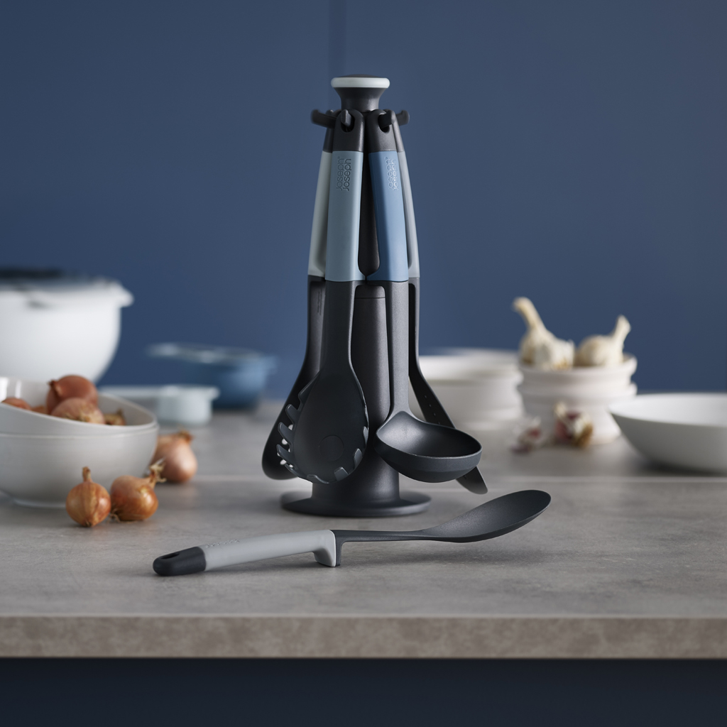 Ein Küchenutensilien-Set mit drehbarem Ständer. Beinhaltet verschiedene Werkzeuge, Zwiebeln, Knoblauch und Schalen. Der Hintergrund ist eine blaue Wand.