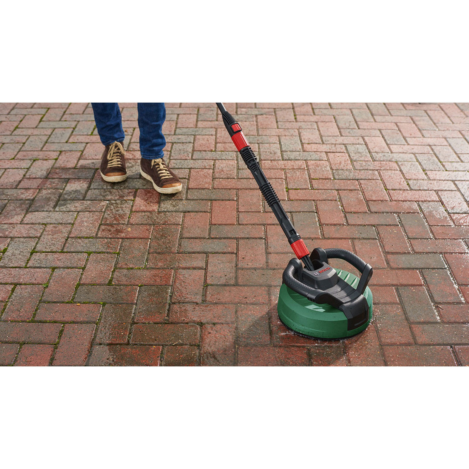 Una persona pulisce un patio in mattoni con un'idropulitrice. La lavatrice è verde e nera.