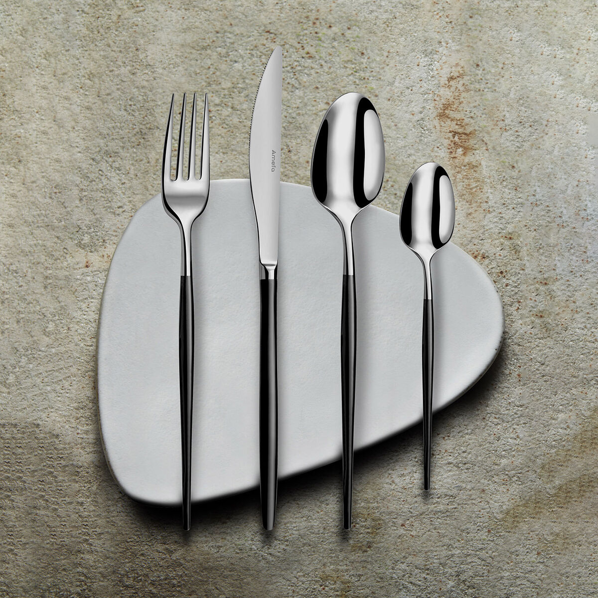 Servizio di posate su piatto bianco: forchetta, coltello, cucchiaio e cucchiaino, con manici neri, su superficie beige strutturata.